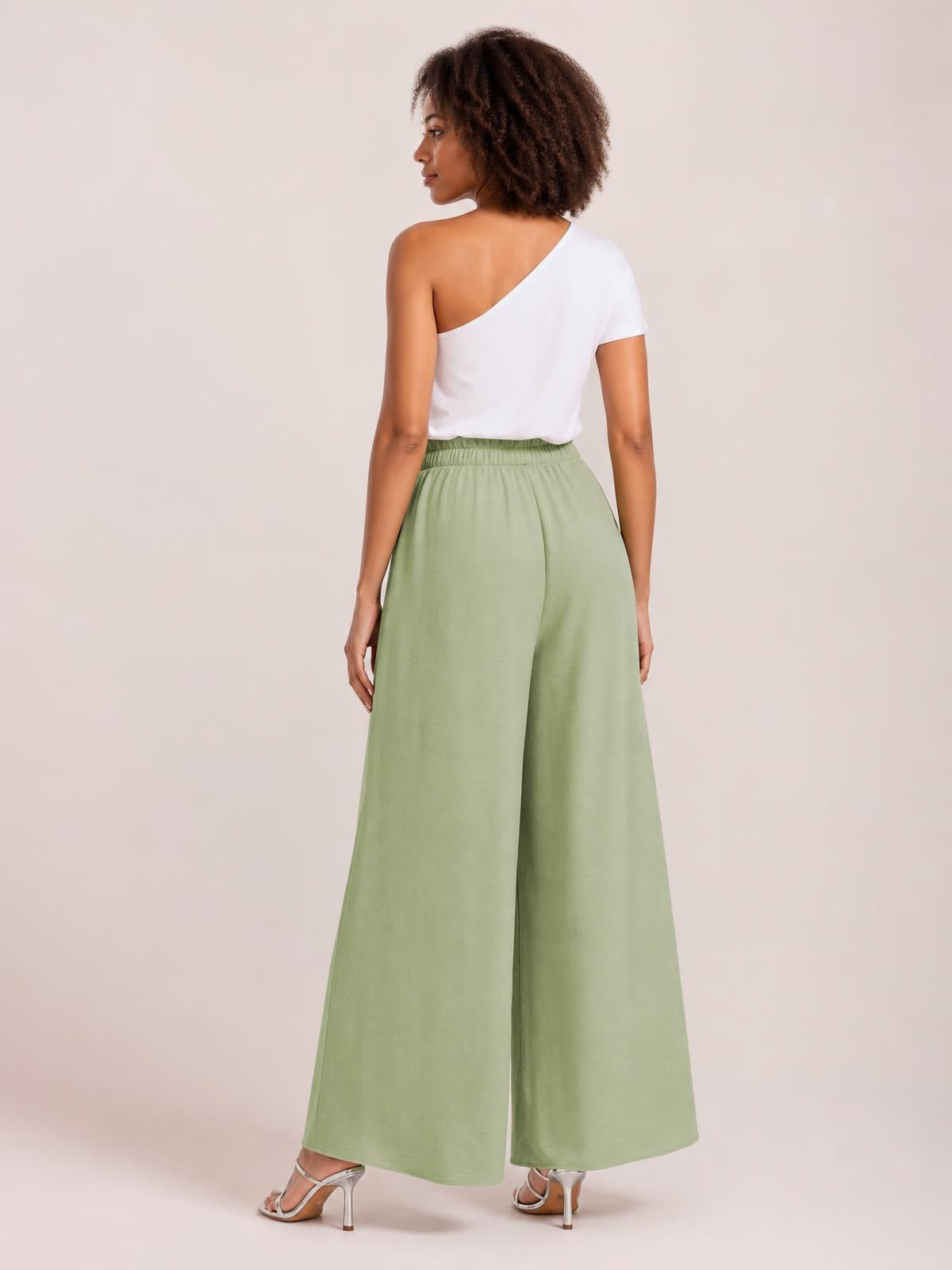 Model viewed from behind wearing sage green tied high waist wide leg pants with an elastic waistband and flowing full-length silhouette.