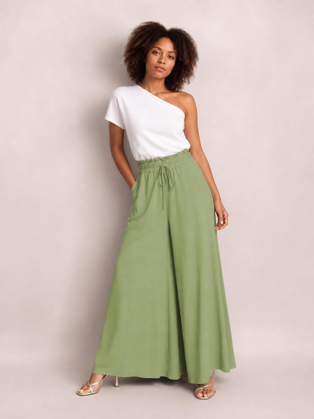 Model poses with one hand in a pocket, wearing sage green high-waist wide-leg pants with a gathered waistband and front tie.