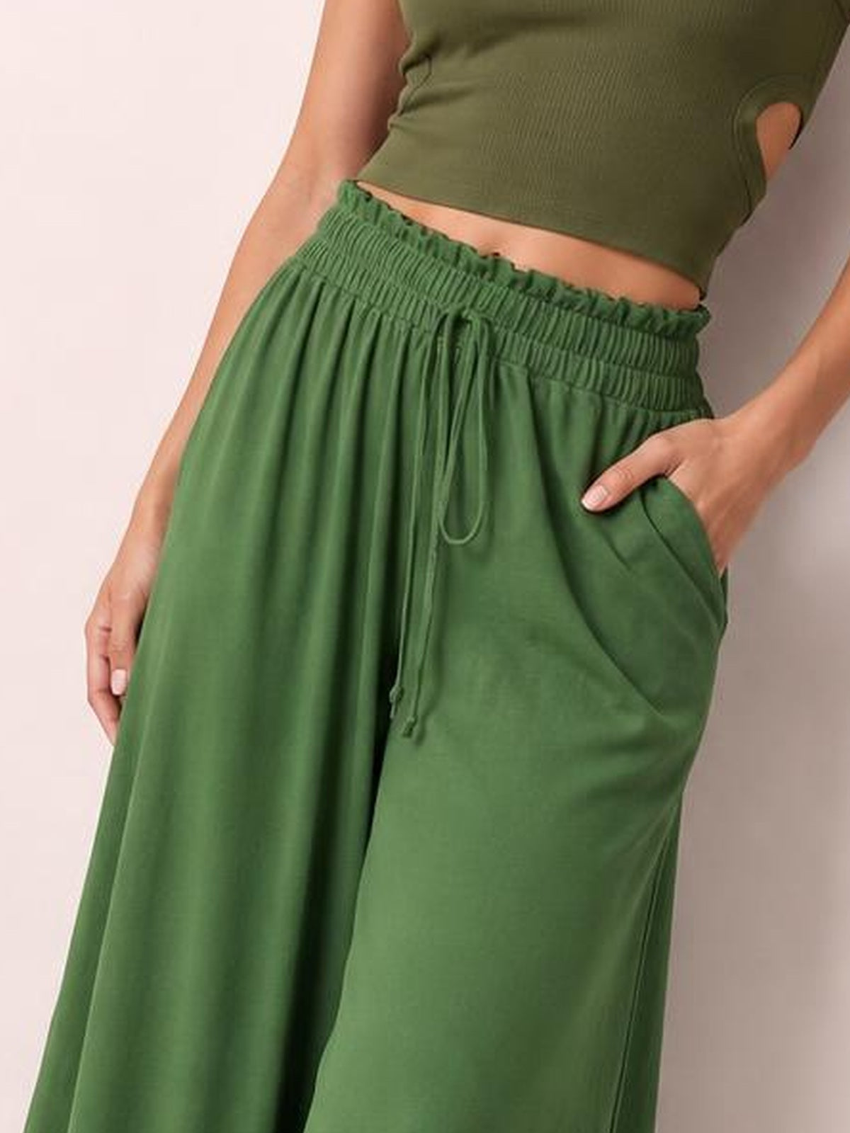 Model wearing green tied high waist wide leg pants with a gathered elastic waistband, drawstring, flowing silhouette, and side pockets.