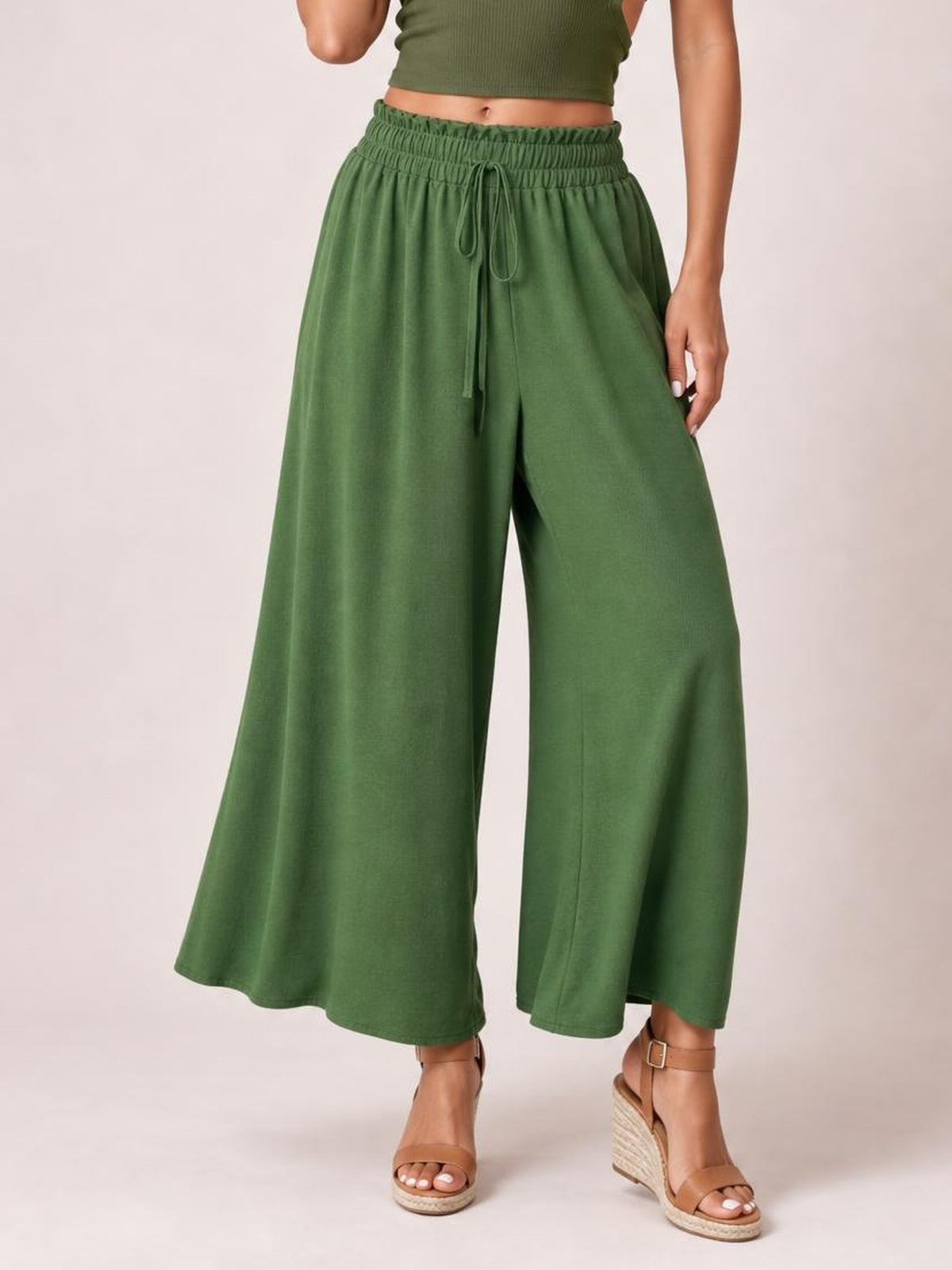 Model wears green tied high-waist wide-leg pants with a gathered waistband, drawstring front, flowing opaque silhouette, and cropped hems.