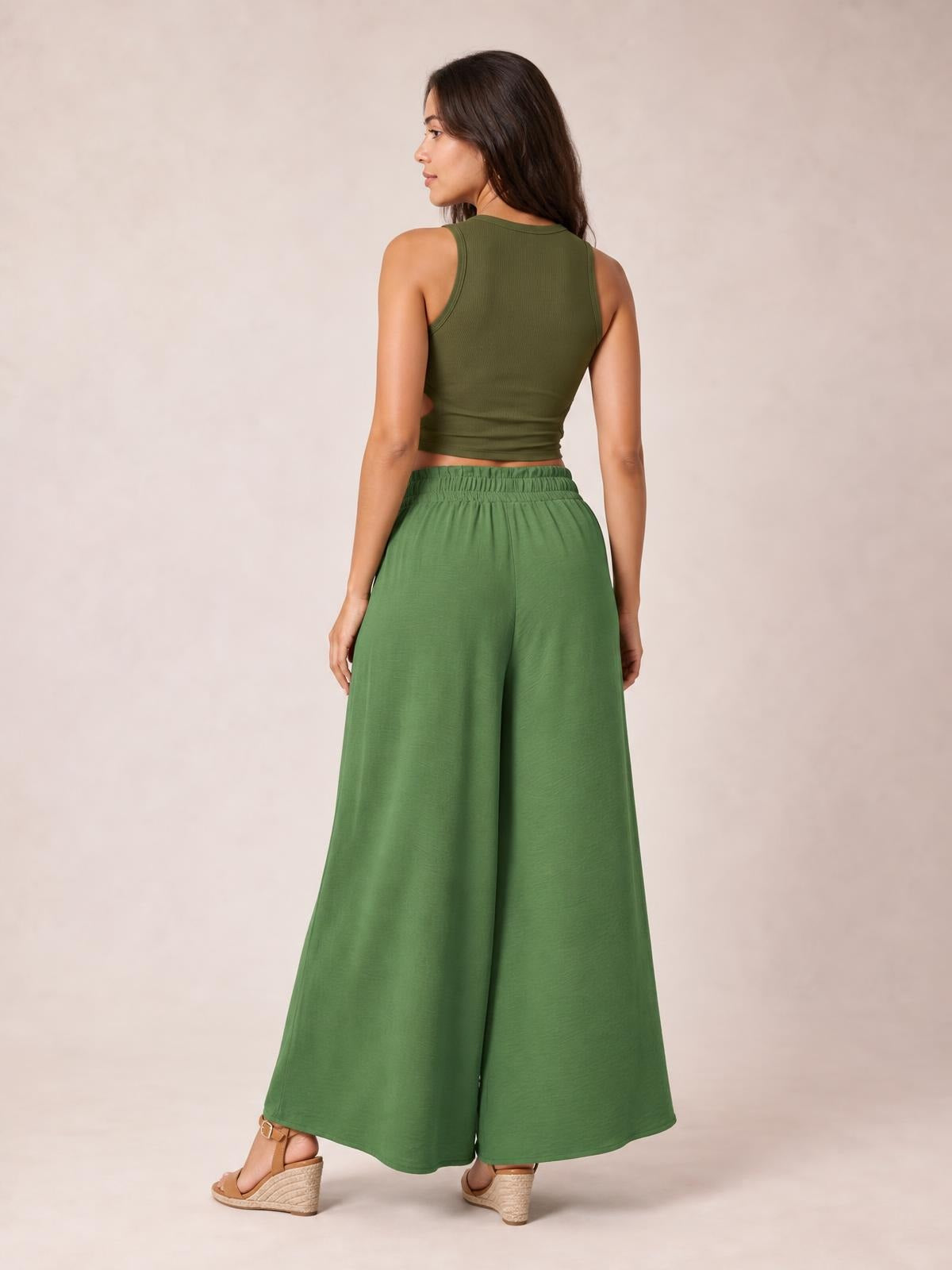 Model poses with her back to the camera in green tied high-waist wide-leg pants featuring an elastic waistband and flowing, full-length silhouette.