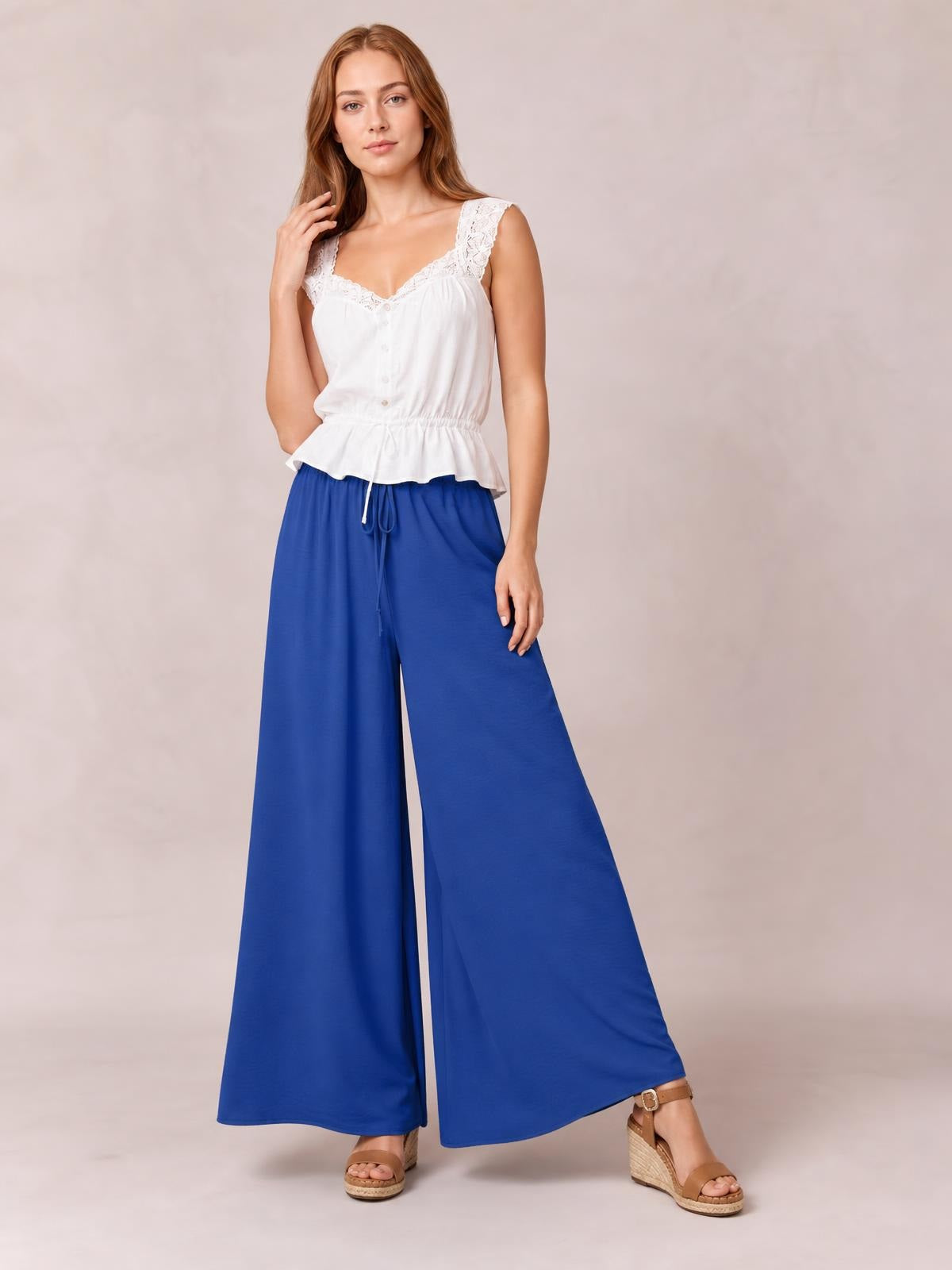 Model poses in vivid blue tied high waist wide leg pants with a fluid full-length silhouette and relaxed, flowing construction.
