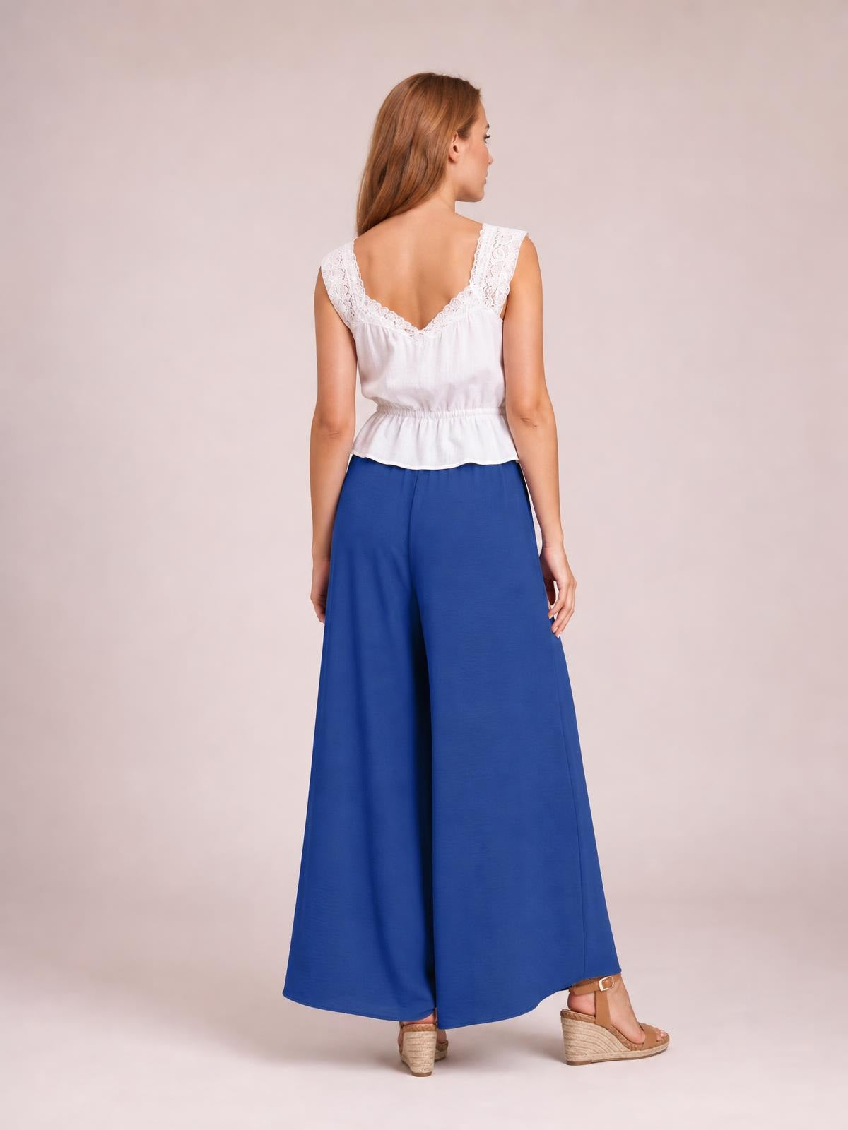 Model shown from behind in a turned pose wears opaque blue high-waist wide-leg pants with a flowing, full-length silhouette and relaxed construction.