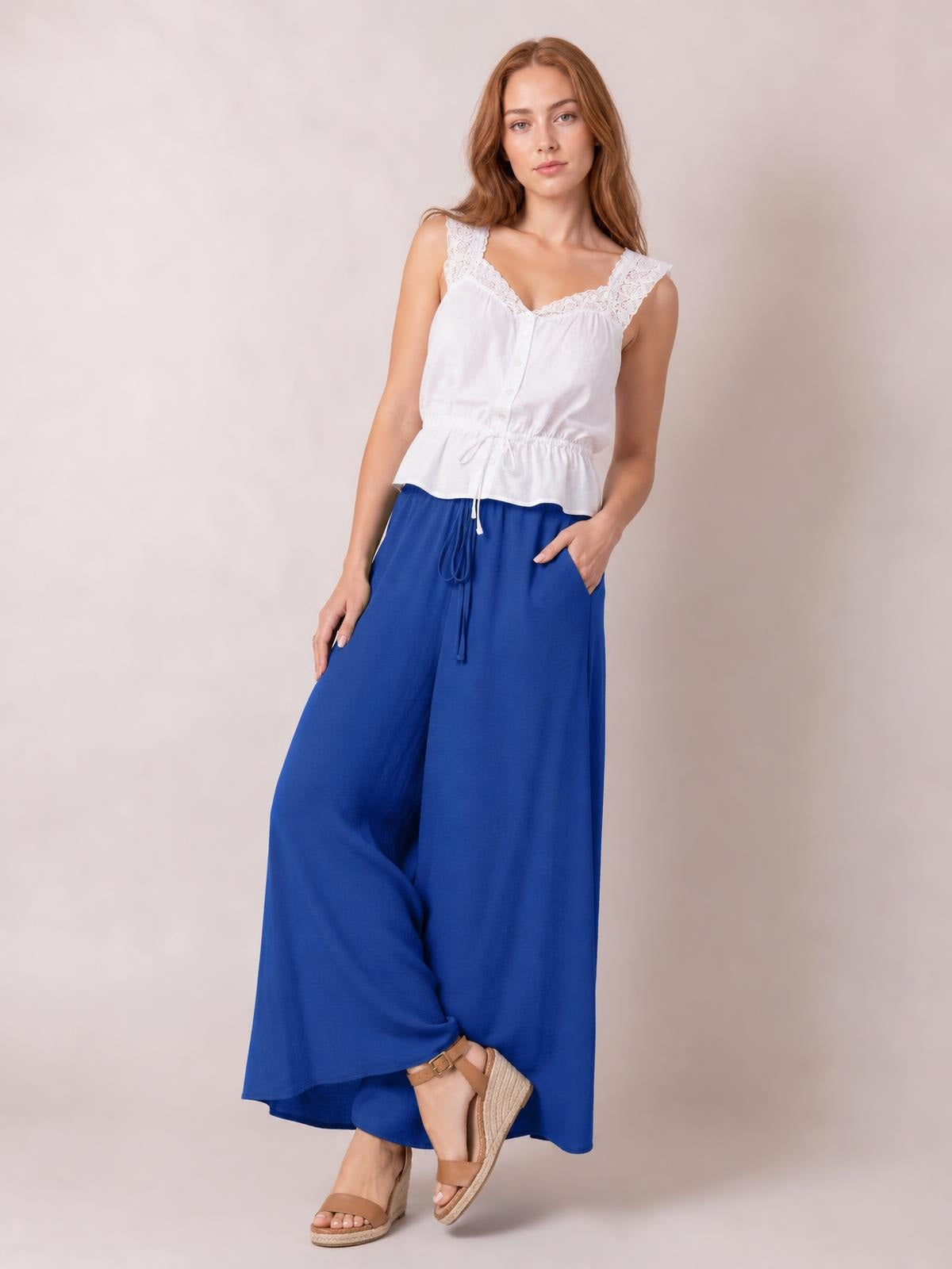 Model poses in royal blue tied high waist wide leg pants with a flowing, loose silhouette and drawstring waist.