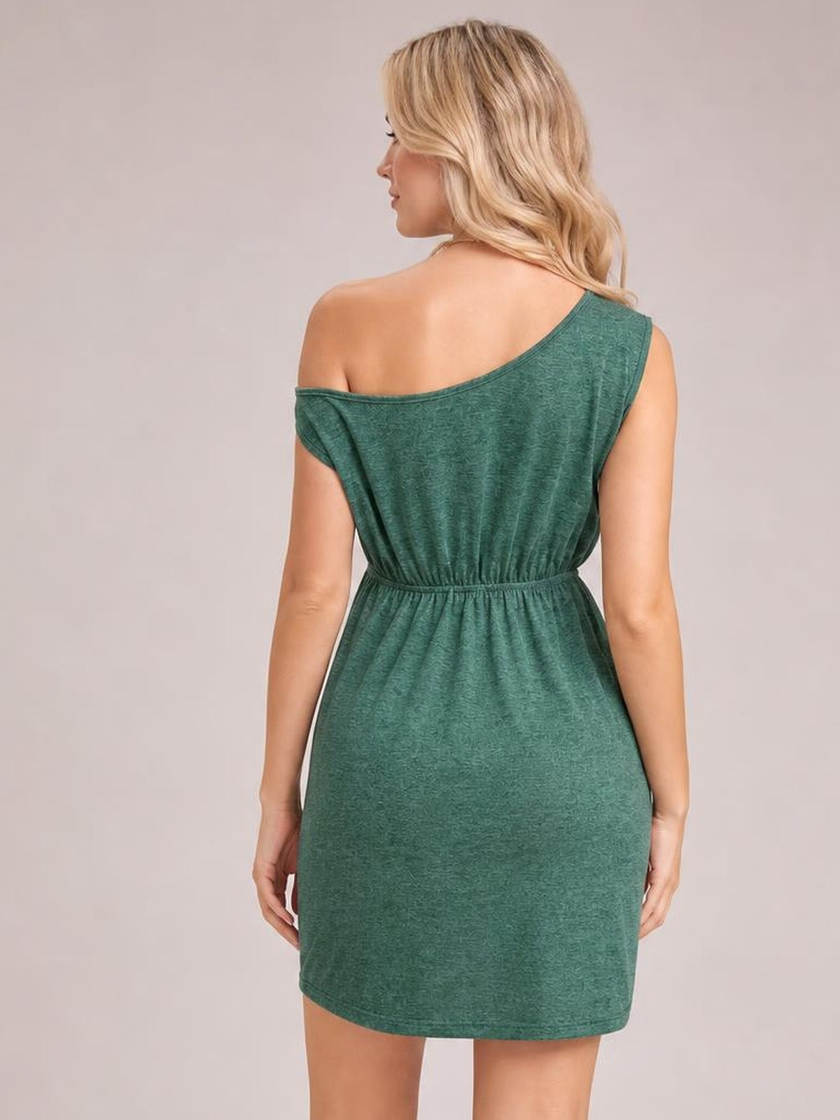 A model stands with her back to the camera in a green single-shoulder sleeveless dress with a gathered waist, relaxed silhouette, and straight mini hem.