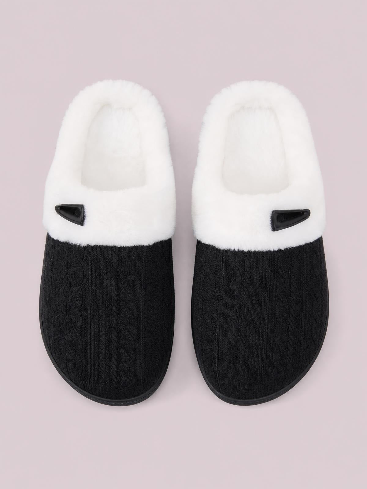 Black flat slippers feature a furry white upper, textured black rounded toes, and a distinctive horn-shaped buckle on each vamp.