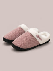 Pink knit flat slippers feature a furry white lining, horn-style buckle detail, rounded toes, and sturdy black rubber soles.