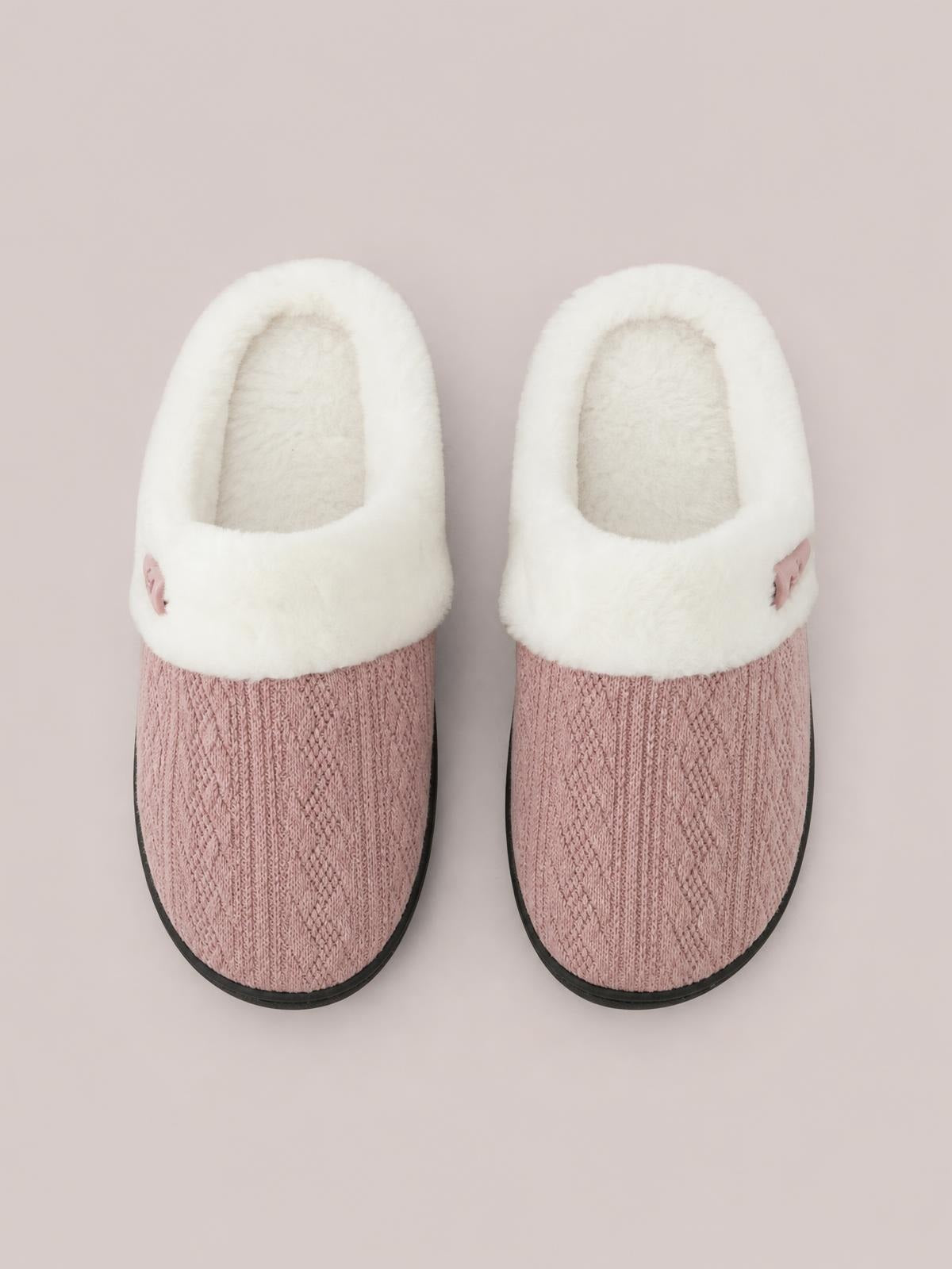 Pink knitted flat slippers feature plush white furry lining, rounded toes, small horn-style buckles at the sides, and black rubber soles.
