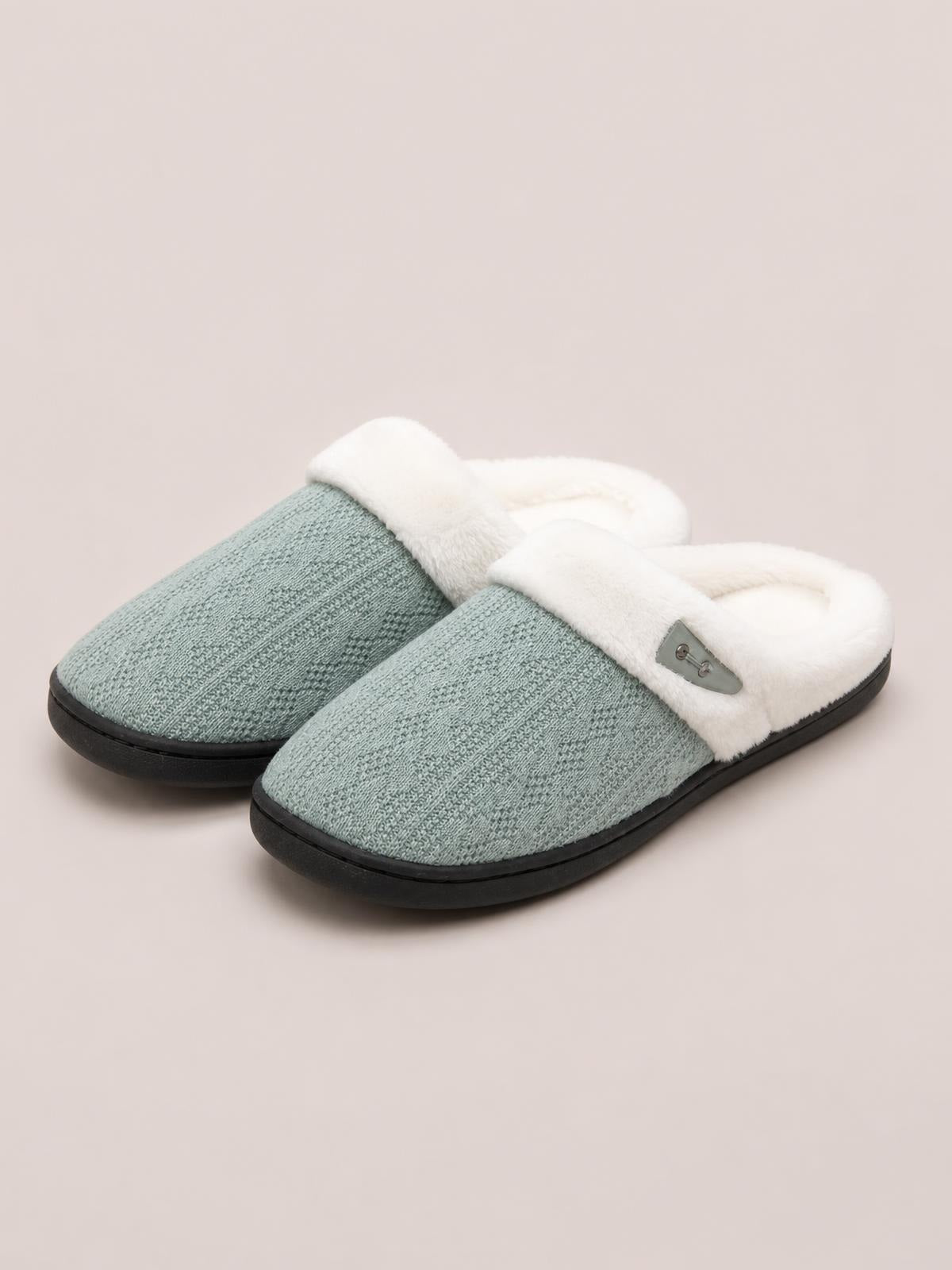 Sage green flat slippers feature a soft furry white lining, textured closed toes, black rubber soles, and a decorative horn buckle accent.