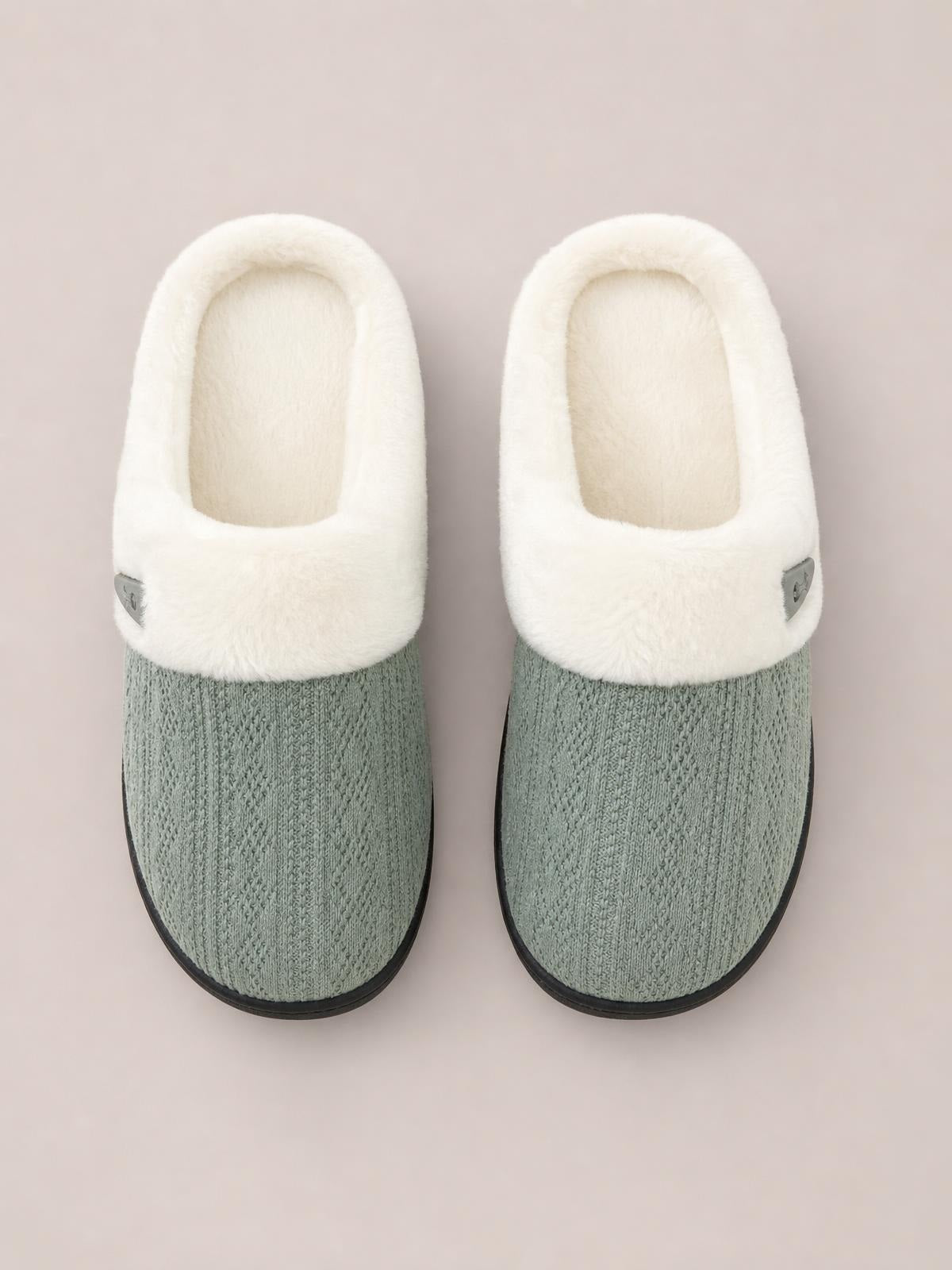A pair of gray-green flat slippers features a textured knit toe, plush white furry uppers, rounded silhouettes, and small side horn-buckle accents.