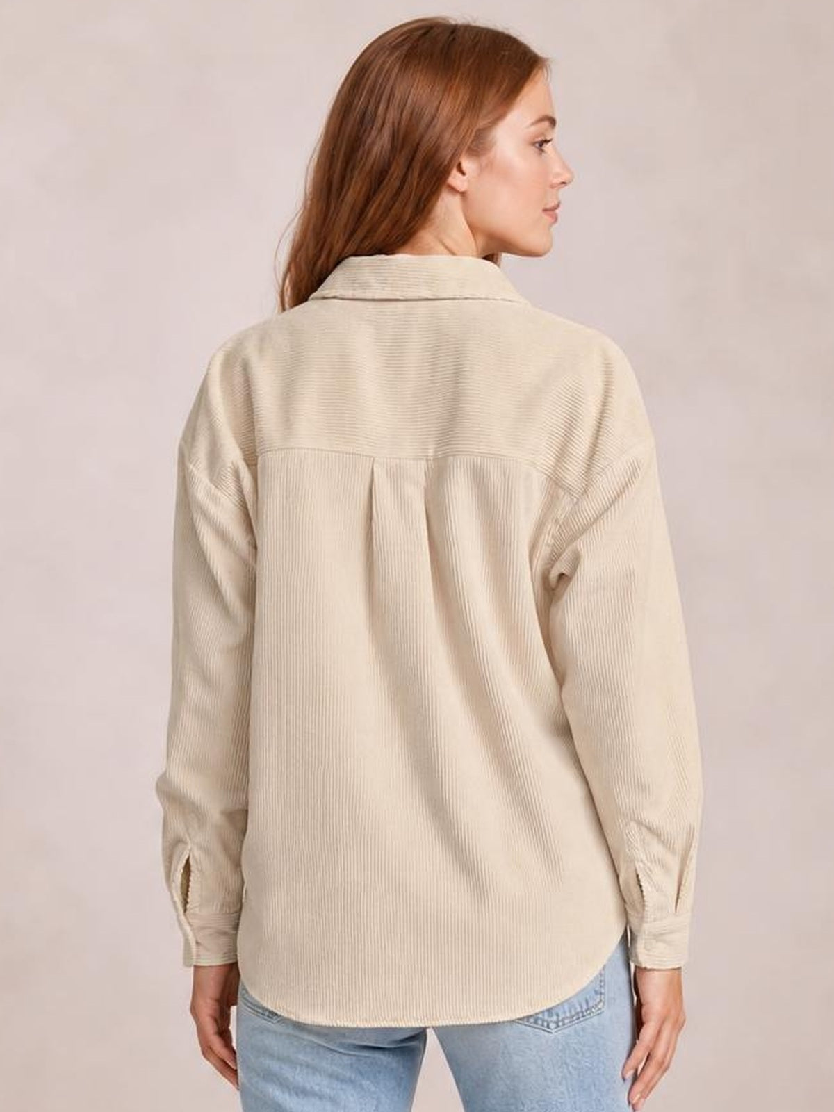 A woman models the back of a beige button-down jacket with a corduroy-like ribbed texture, spread collar, long sleeves, pleated yoke, and relaxed curved-hem silhouette.