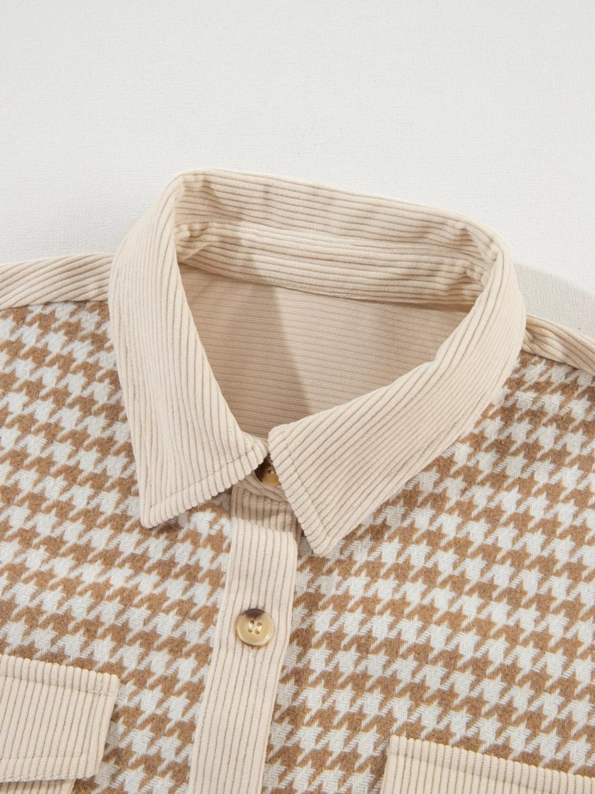 Close-up of a tan and cream houndstooth button-down jacket featuring a ribbed corduroy collar, matching cuffs, and a front button closure.