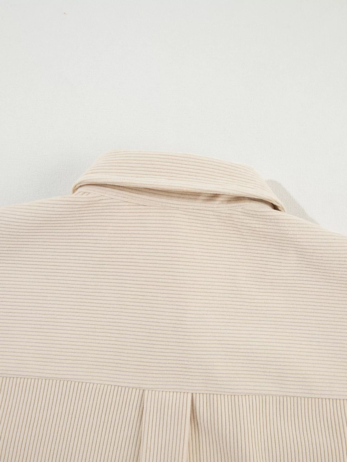 Close-up of a light beige striped jacket showing the collar, back yoke, horizontal fabric texture, and relaxed straight silhouette.