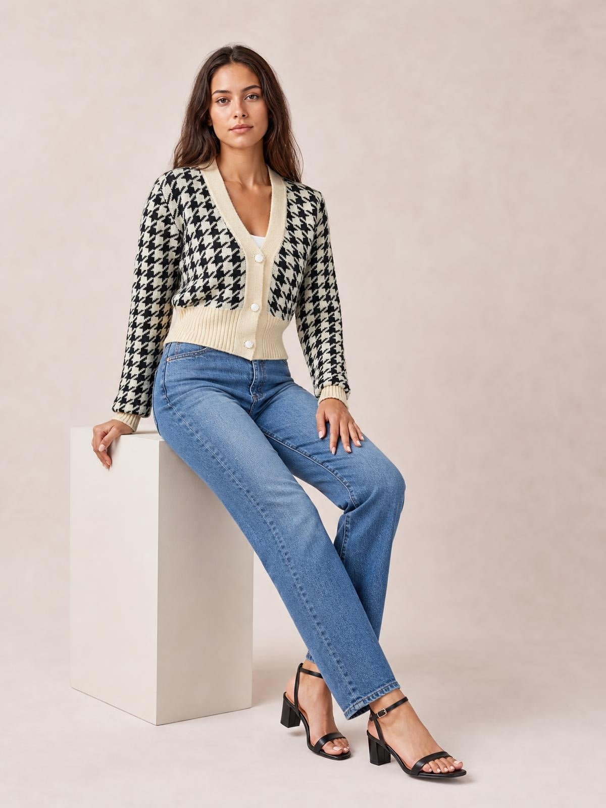 Model seated and wearing a black-and-cream houndstooth button-up long-sleeve cardigan with a V-neck, ribbed trim, and fitted waist.