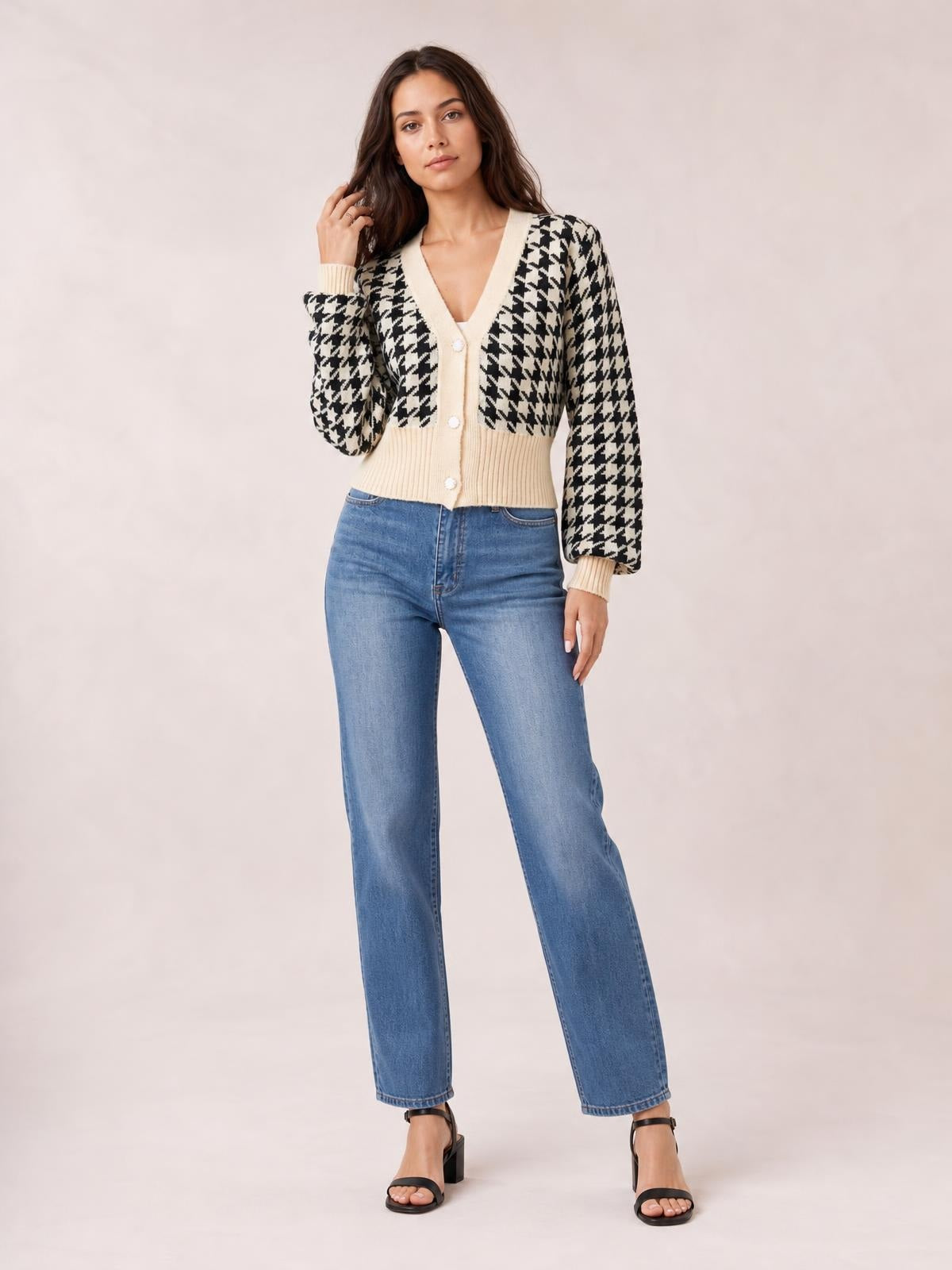 Model poses in a black-and-white houndstooth button-up cardigan with long sleeves, cream ribbed trim, V-neck, and a fitted cropped silhouette.