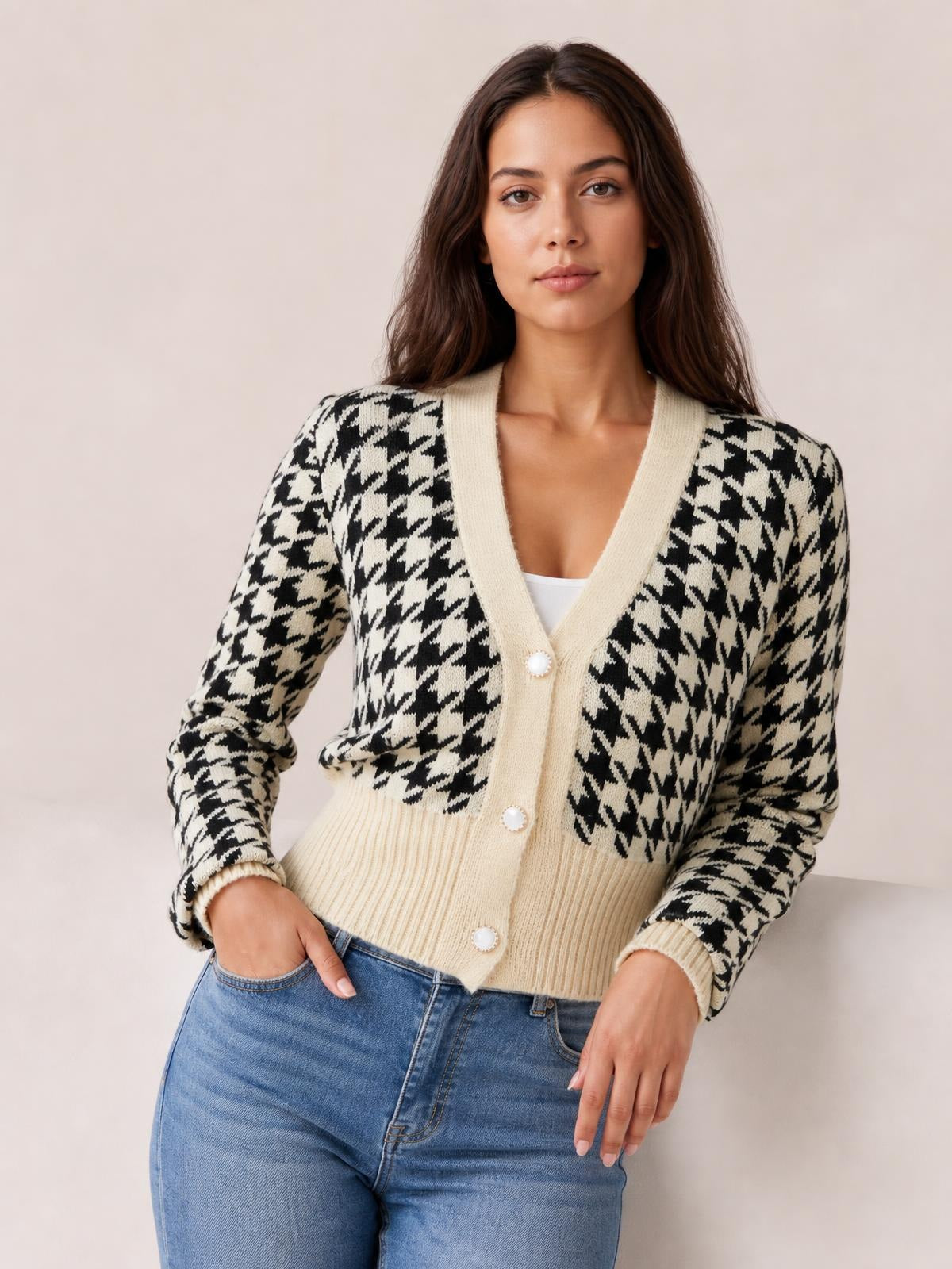 Model poses with one hand in her jeans pocket wearing a black-and-cream houndstooth button-up cardigan with long sleeves, a V-neck, and ribbed trim.