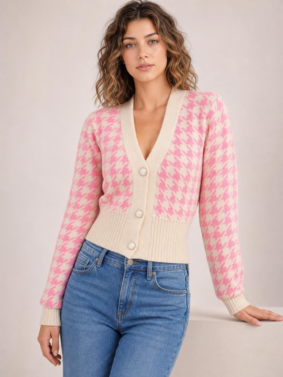 Model wears a pink and cream houndstooth button-up long-sleeve cardigan with a V-neck, pearl-style buttons, ribbed trim, and fitted cropped silhouette.