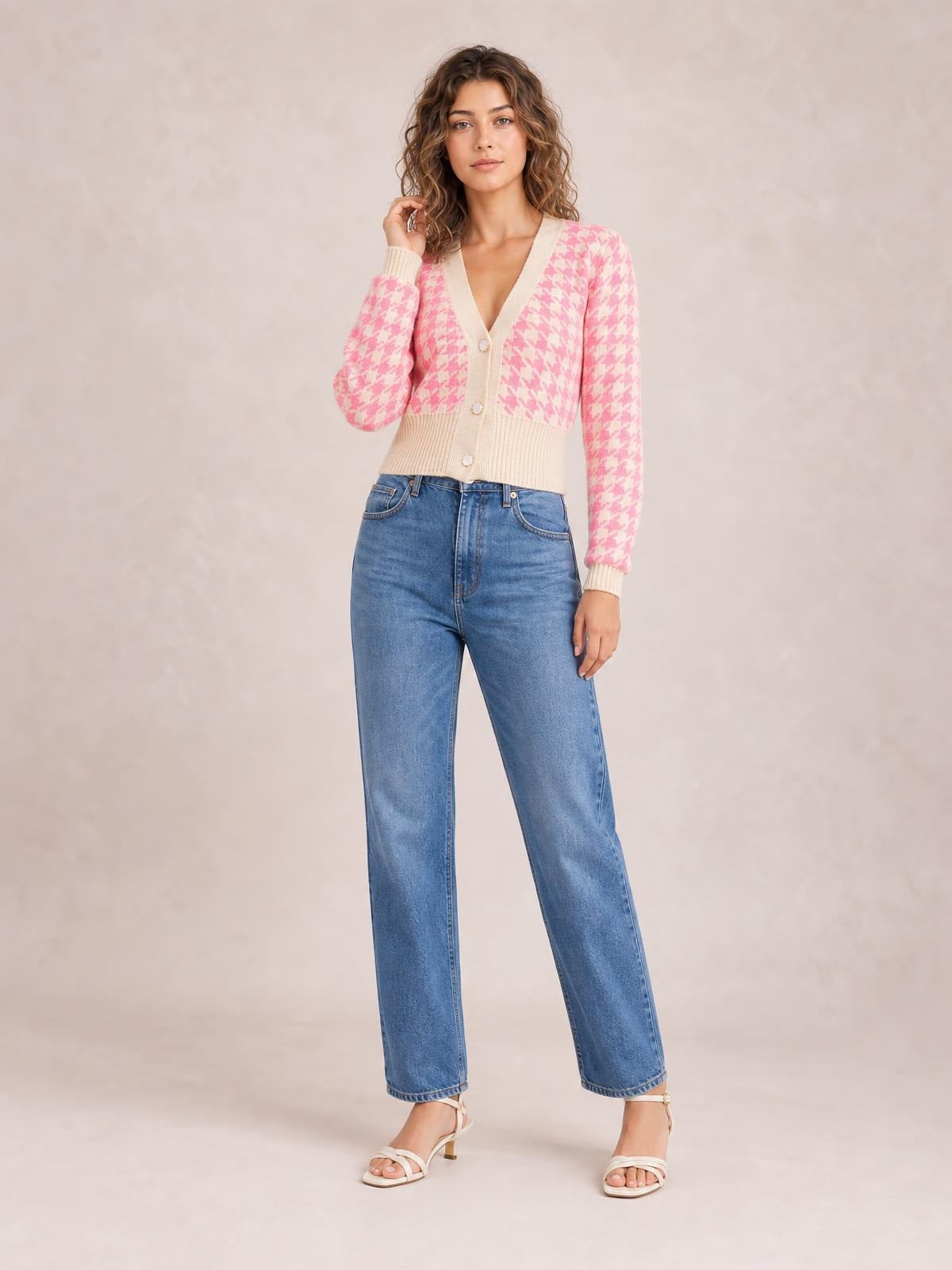 A model poses in a pink and cream houndstooth button-up cardigan with long sleeves, a V-neck, ribbed trim, and a cropped fitted silhouette.