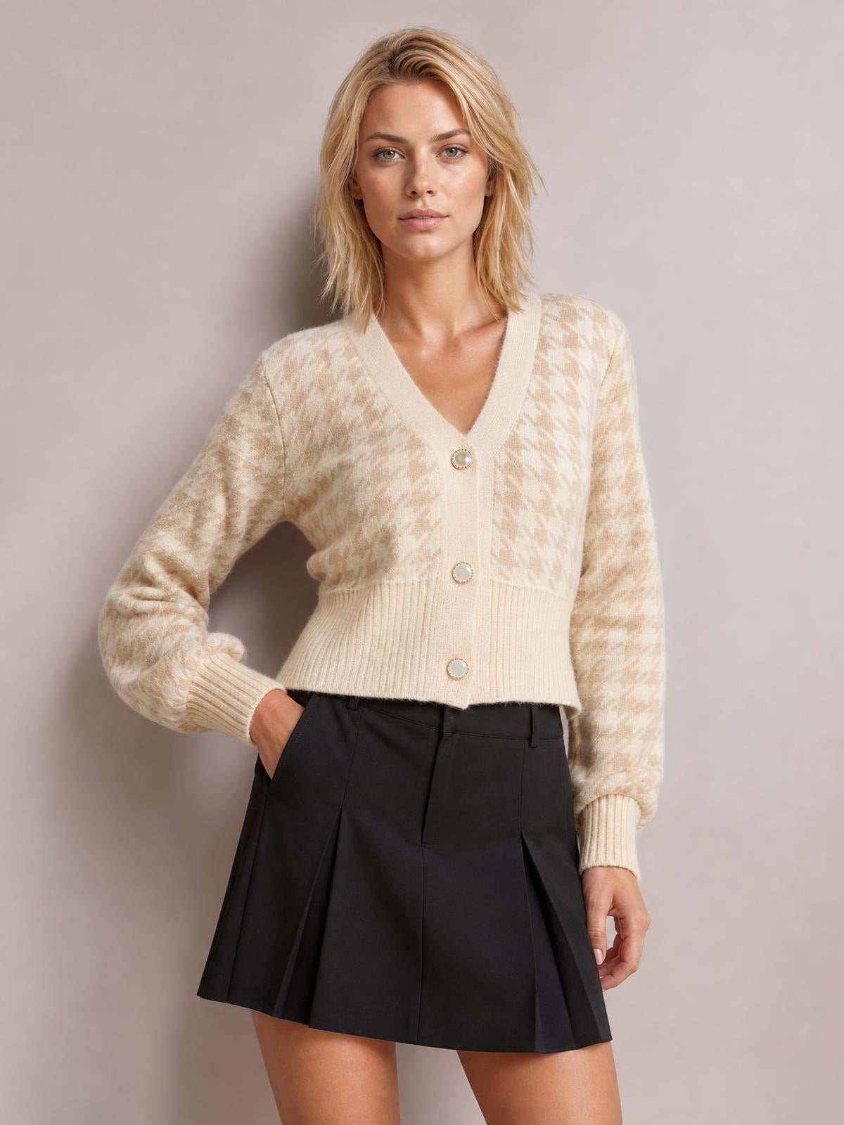 Model poses with one hand in her pocket wearing a cream houndstooth button-up cardigan with a V-neck, long sleeves, ribbed cuffs, and fitted waist-length silhouette.
