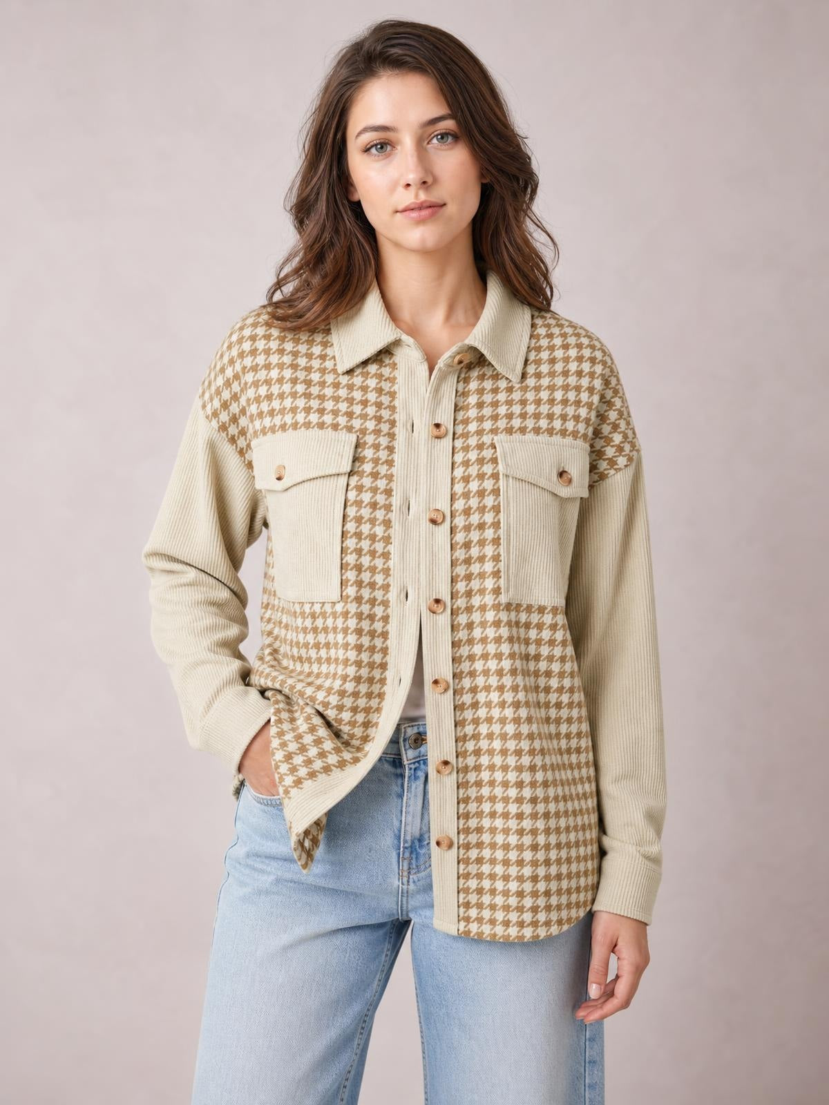 Model poses in a beige and brown houndstooth button-up jacket with long sleeves, a relaxed silhouette, contrasting ribbed panels, collar, and two flap pockets.