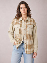 Model poses in a beige and brown houndstooth button-up jacket with long sleeves, a relaxed silhouette, contrasting ribbed panels, collar, and two flap pockets.