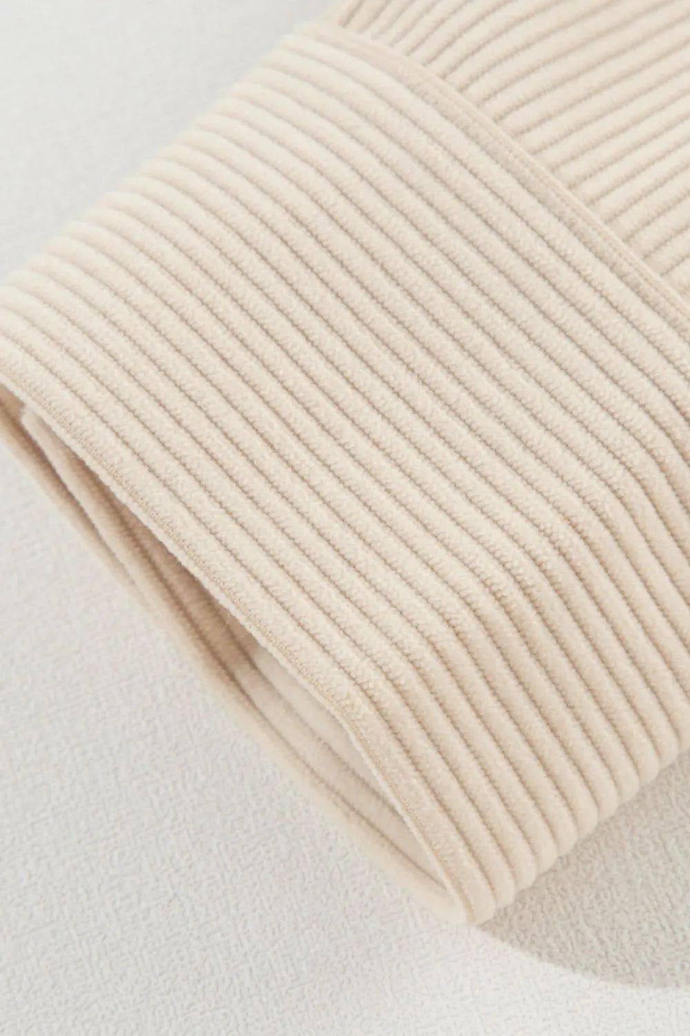 Close-up of a cream long sleeve jacket cuff showing its soft ribbed texture, folded edge, and neatly constructed seam detail.