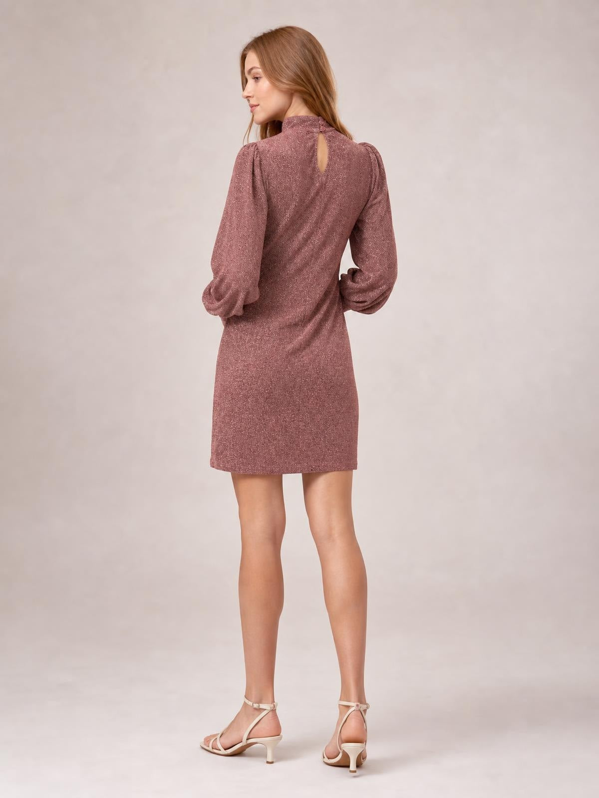 Model shows the back of a mauve glitter mini dress with a mock neck, keyhole closure, long bishop sleeves, and a straight, figure-skimming silhouette.