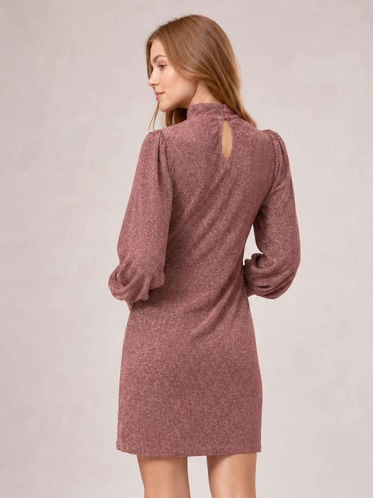 Model poses in a mauve glitter mini dress with a mock neck, back keyhole closure, long bishop sleeves, and a straight silhouette.