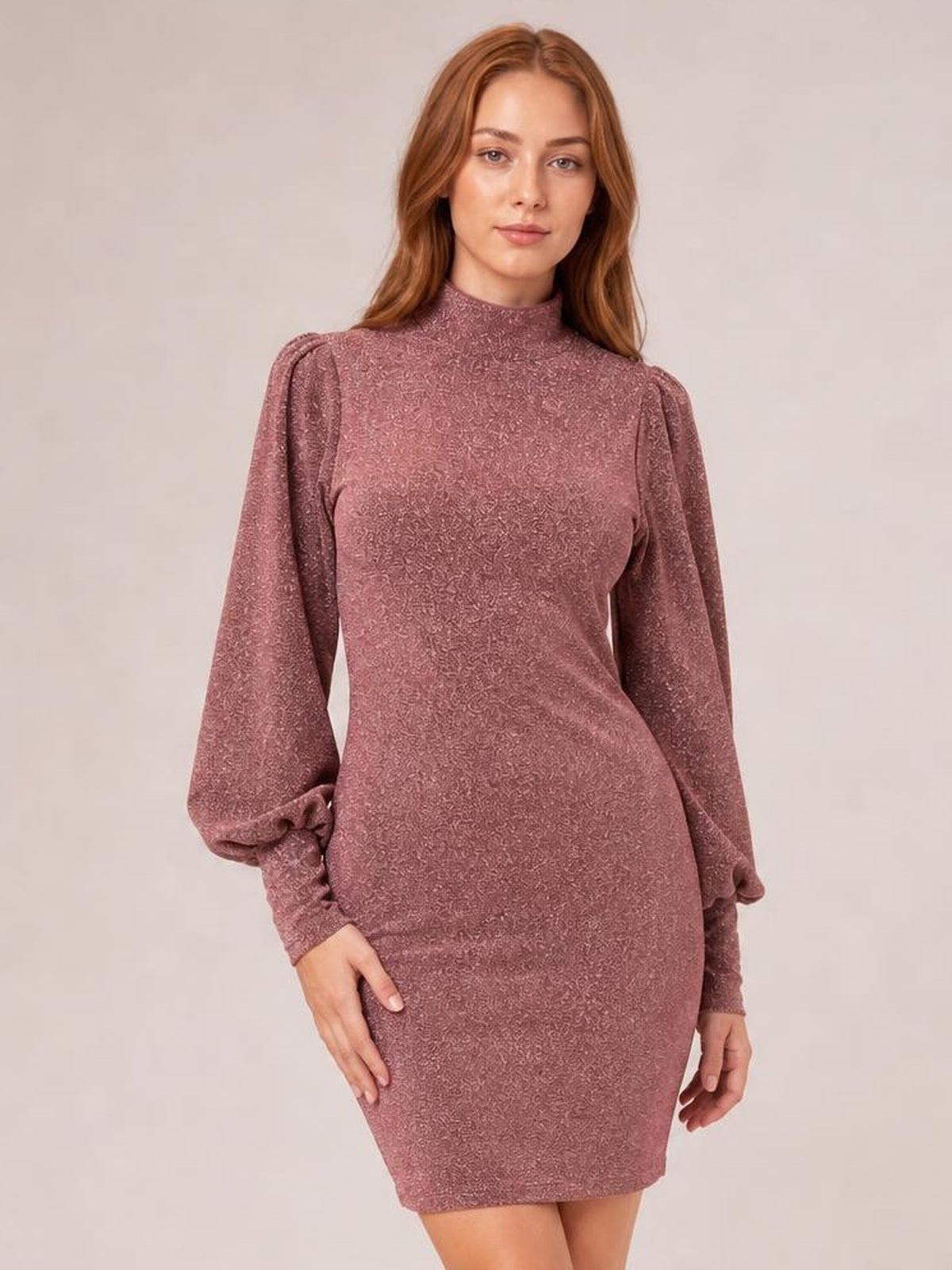 Model poses in a mauve glitter knit mini dress with a figure-hugging silhouette, mock neck, long bishop sleeves, and gathered cuffs.