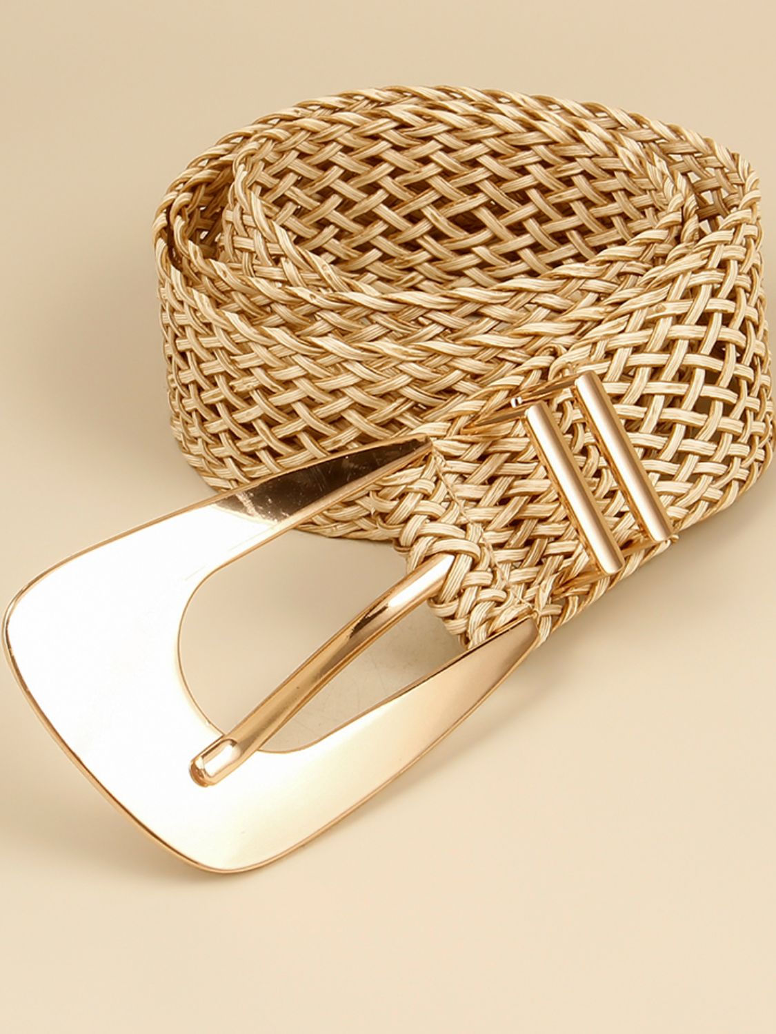 A tan braided polyester belt features a wide woven silhouette and an elongated polished gold-tone alloy buckle with an irregular statement shape.