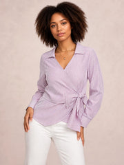Model poses in a pink-and-white striped blouse with a Johnny collar, long sleeves, wrap-style front, and bow tie waist creating a flattering silhouette.