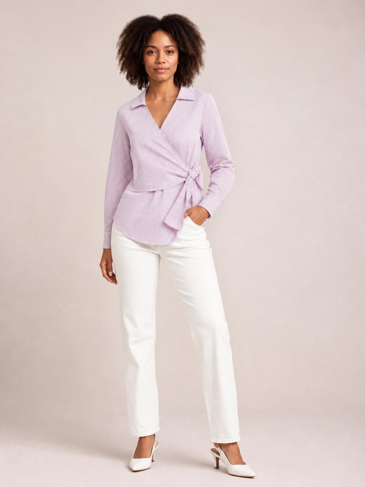 Model stands in a pink-and-white striped blouse with a Johnny collar, long sleeves, curved hem, and a bow-tie waist creating a polished silhouette.