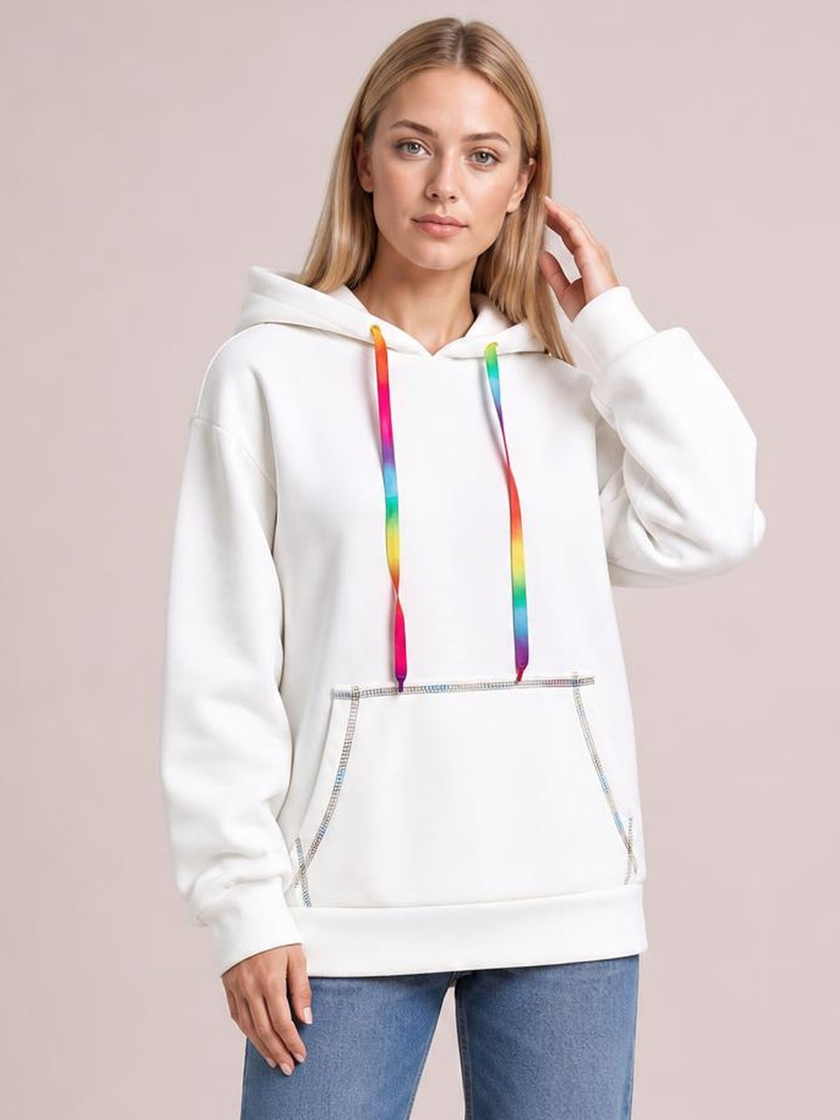 A woman poses in a relaxed white hoodie with colorful drawstrings, raglan sleeves, contrast stitching, a roomy silhouette, and a front kangaroo pocket.