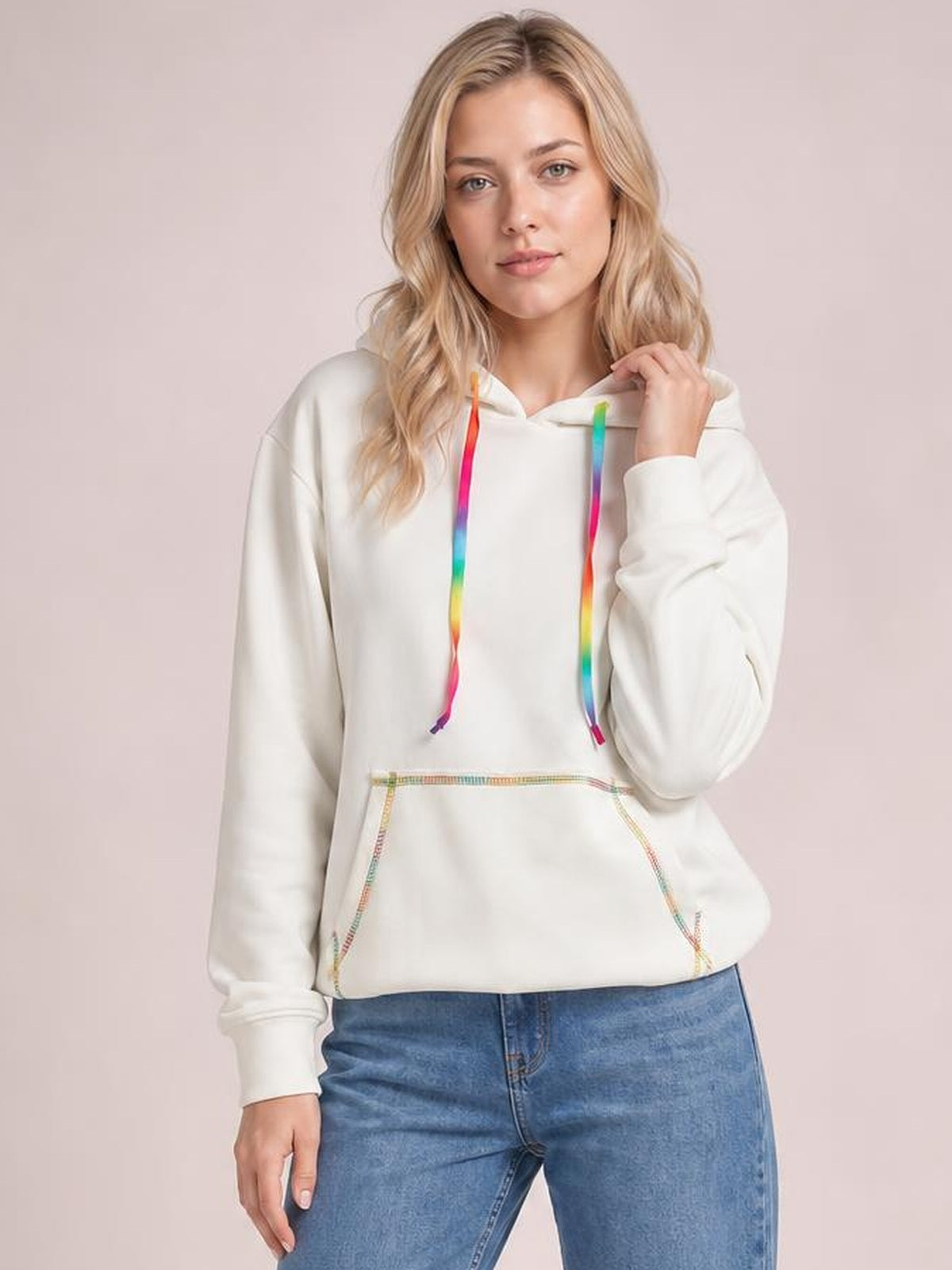 A model wears a white drawstring hoodie with raglan sleeves, colorful contrast stitching, rainbow cords, and a relaxed silhouette while holding the hood.