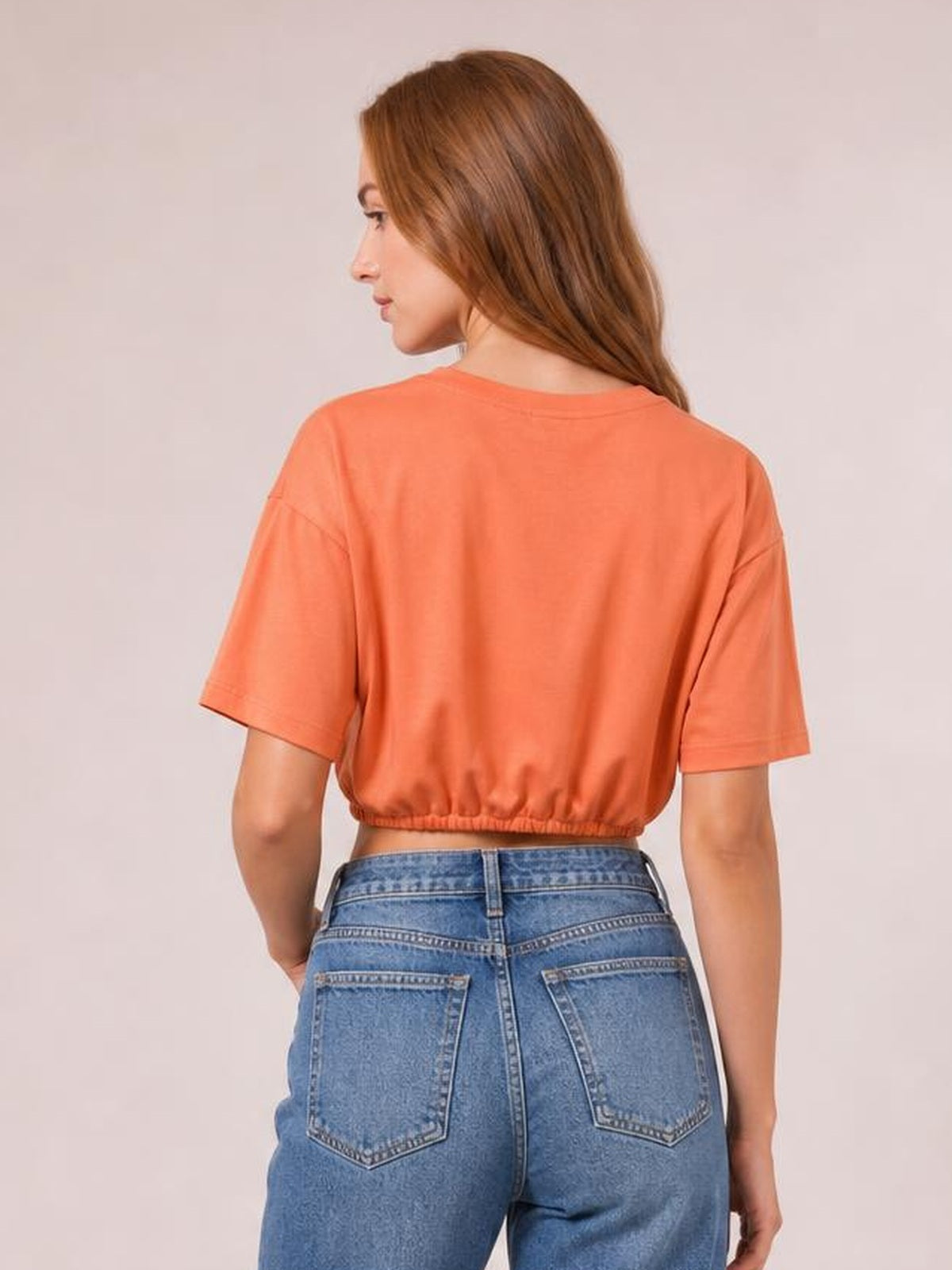 A model looks over her shoulder wearing a coral drawstring round-neck short-sleeve T-shirt with a relaxed cropped silhouette and gathered hem.