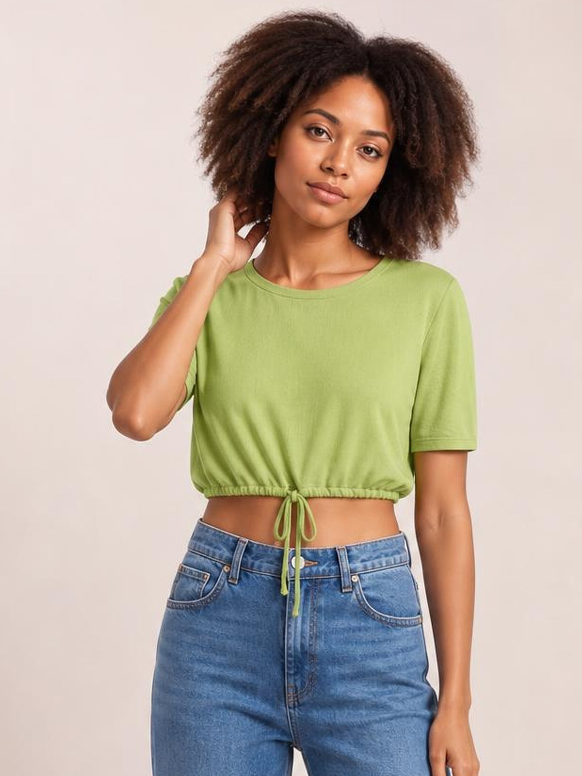 A model poses with one hand in her hair wearing a lime green round-neck short-sleeve T-shirt with a cropped drawstring hem.
