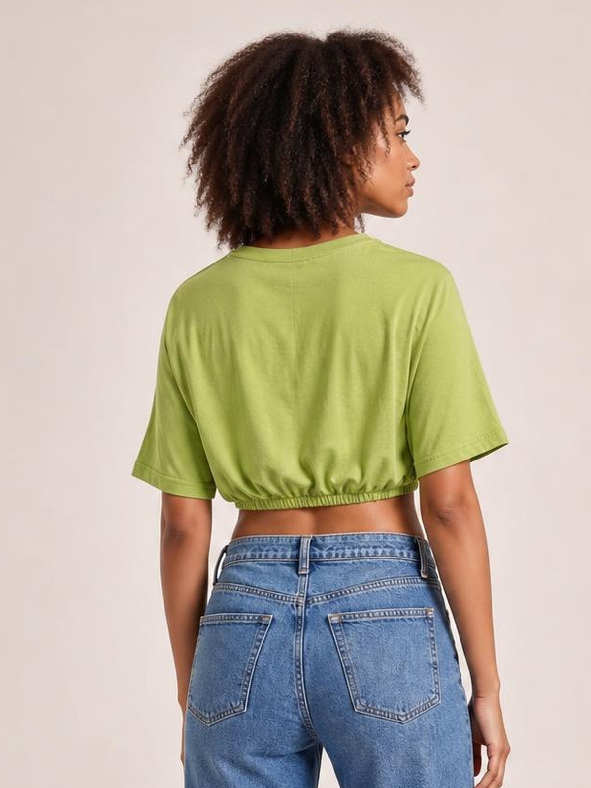 A model shown from the back wears a lime green drawstring round-neck short-sleeve T-shirt with a cropped, gathered hem and relaxed silhouette.