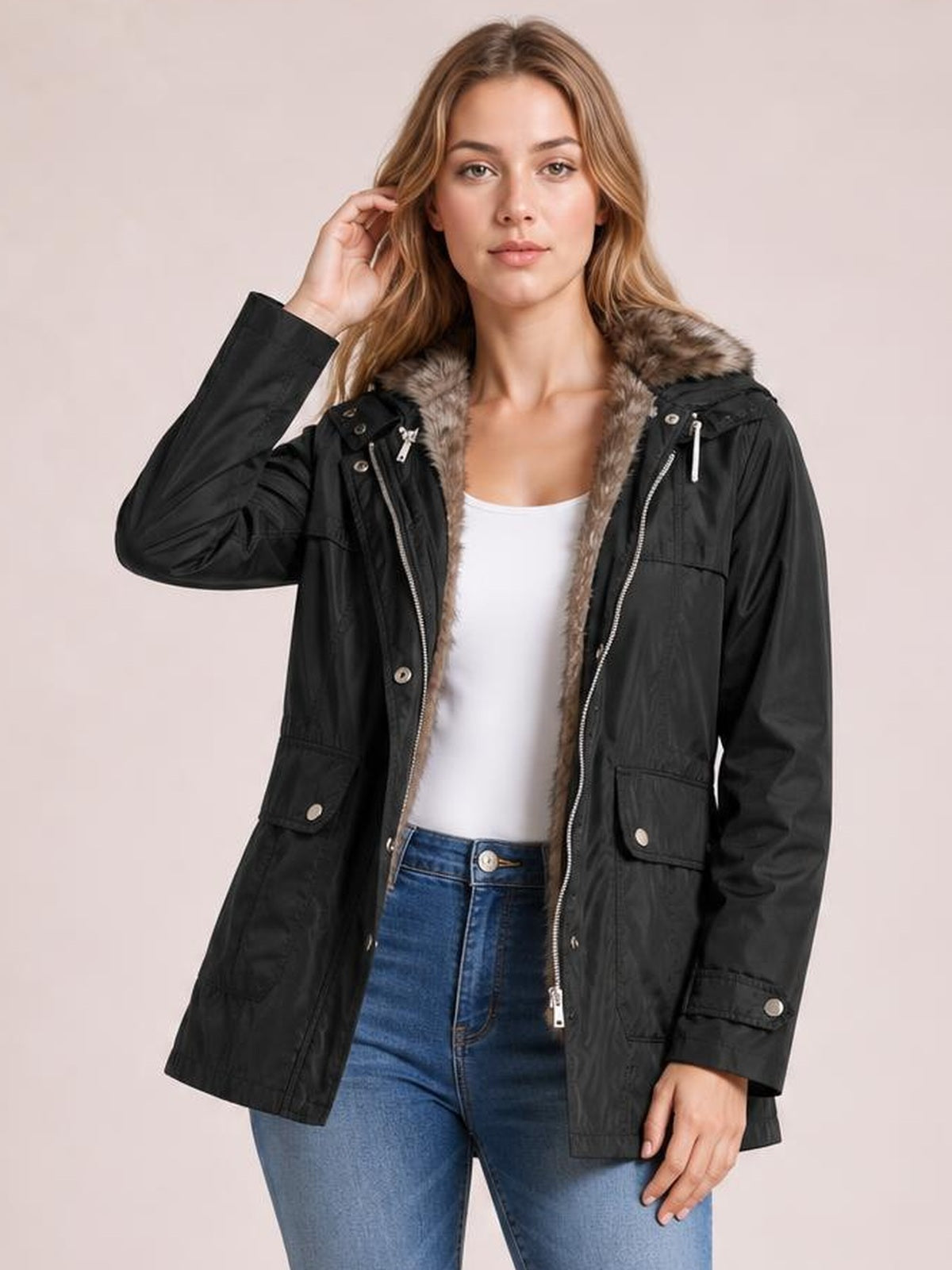Model poses in a black hooded jacket with a plush faux-fur-lined collar, zip-and-button front, flap pockets, and a relaxed hip-length silhouette.