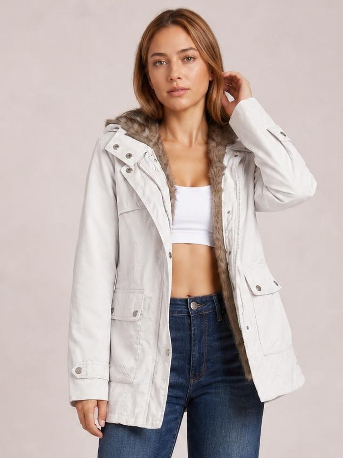 Model wears a white hooded jacket with a visible faux-fur detachable liner, buttoned flap pockets, long sleeves, and a relaxed mid-thigh silhouette.