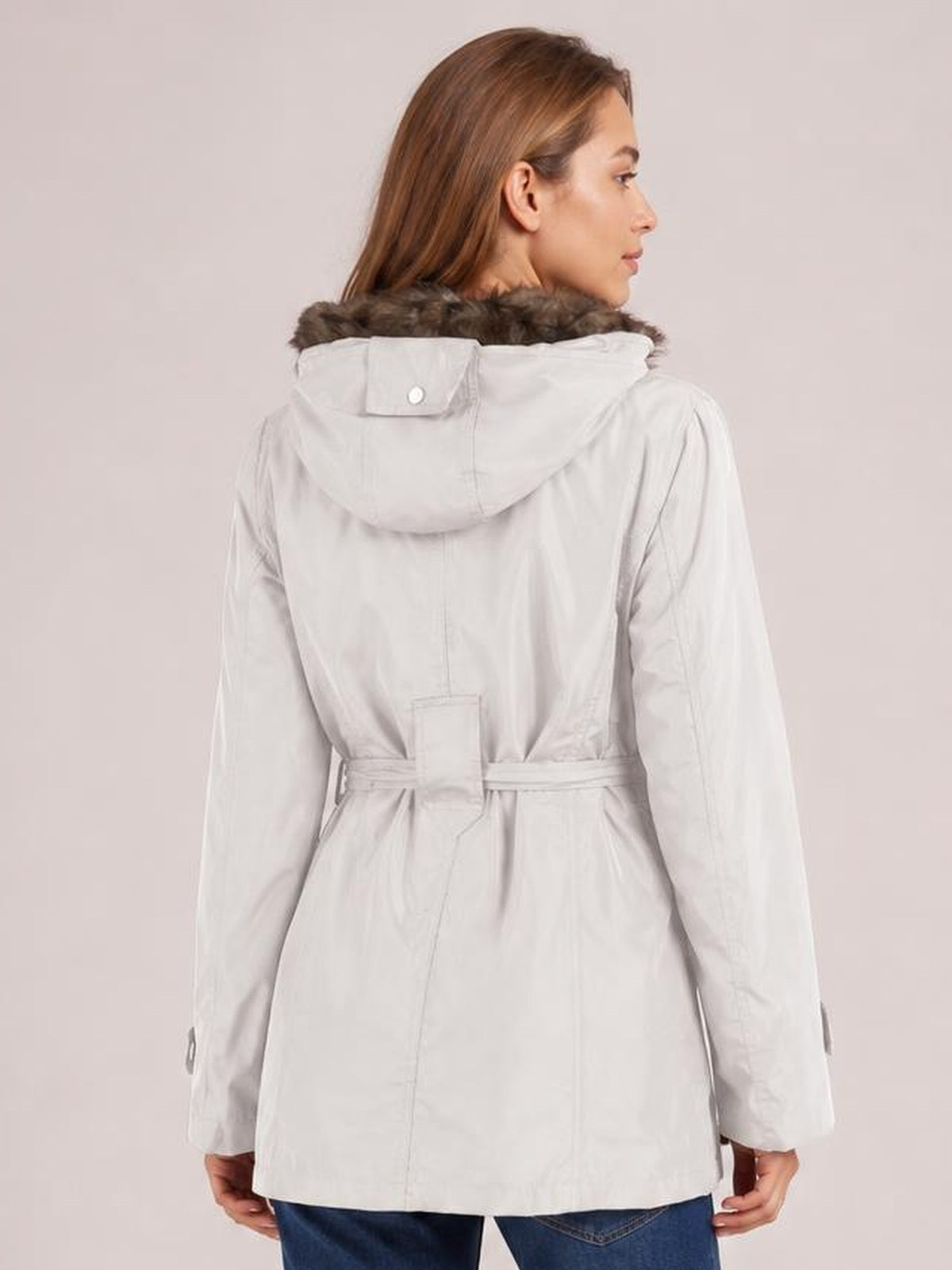Model shown from behind wears a white hooded jacket with faux-fur trim, long sleeves, buttoned hood flap, cinched waist belt, and relaxed mid-thigh silhouette.