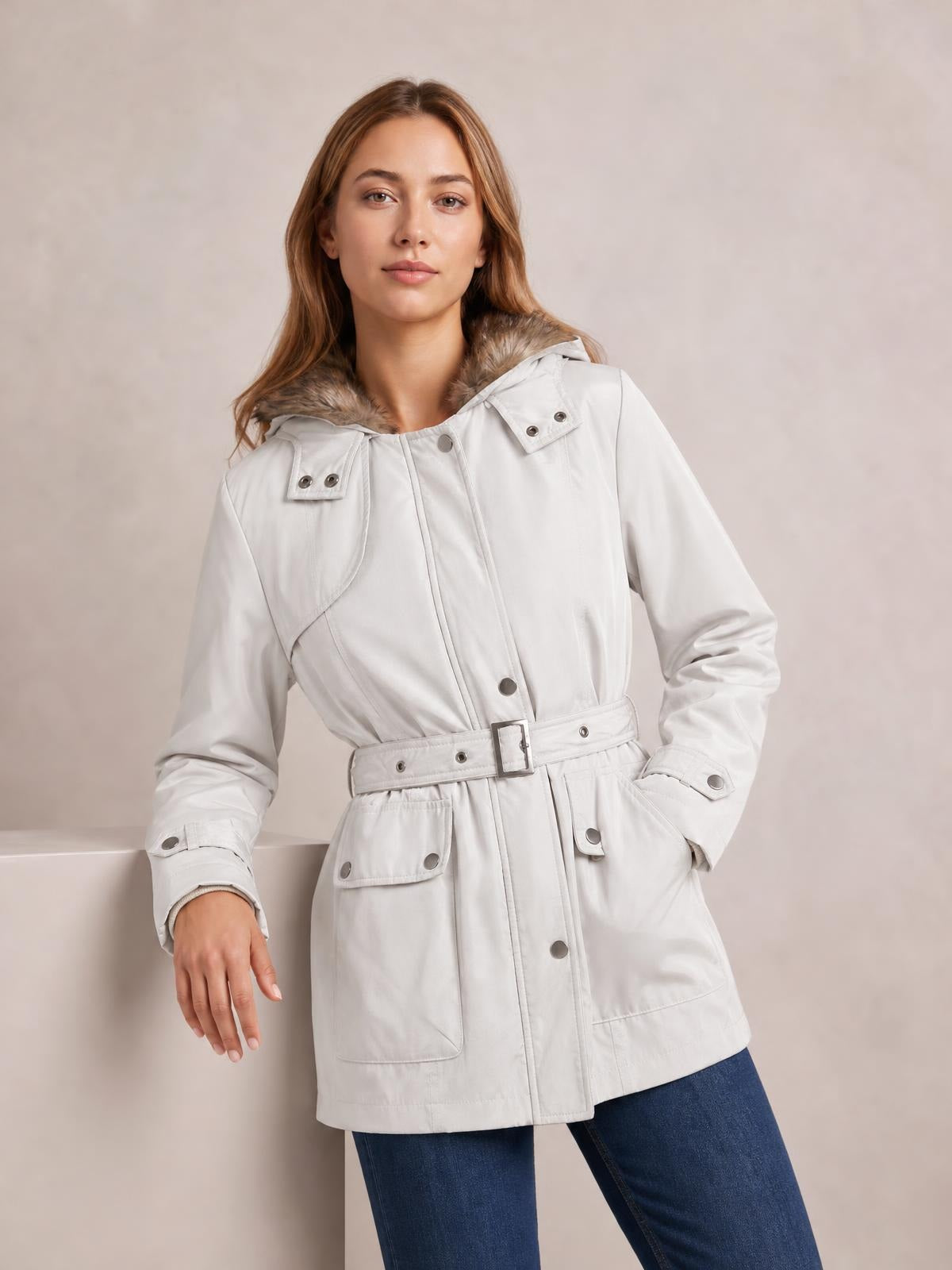 Model poses in a white hooded jacket with a faux-fur-trimmed detachable liner, button front, belted waist, and multiple flap pockets.