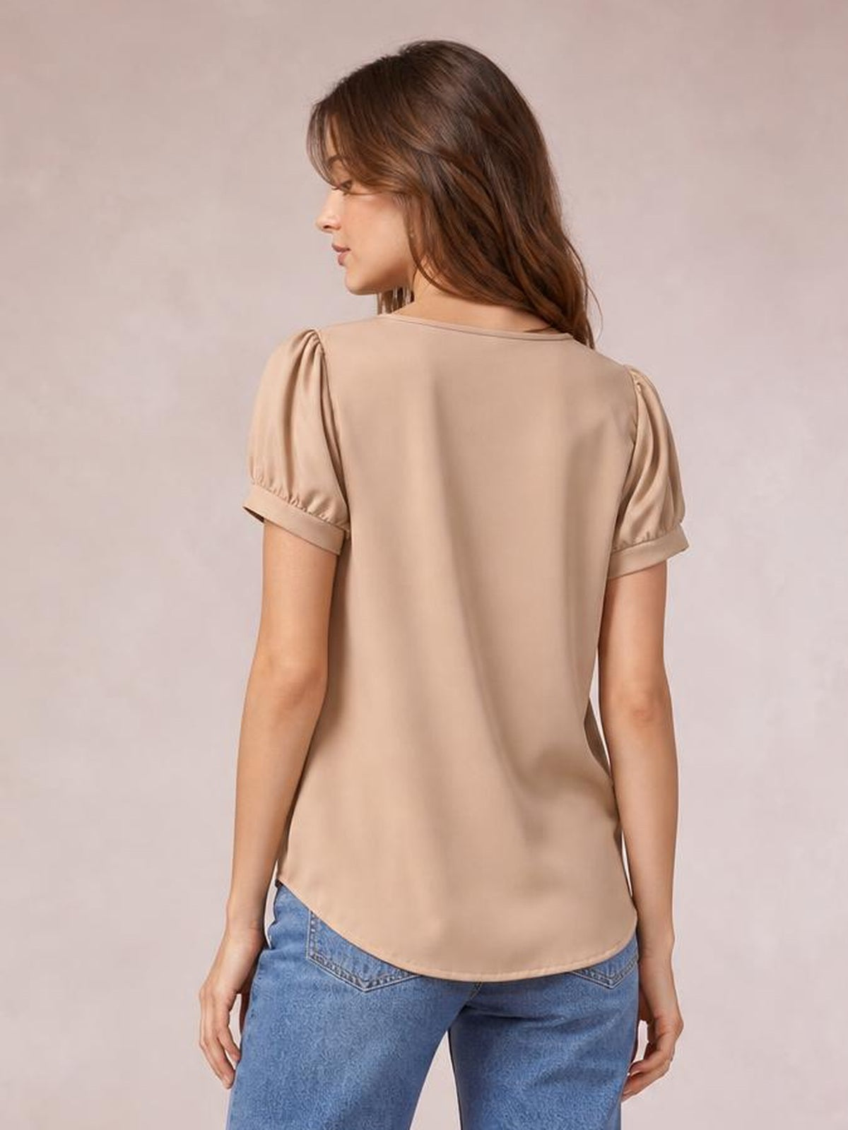 Model shown from behind wearing a beige blouse with short ruched puff sleeves, a relaxed silhouette, and a rounded hem over blue jeans.