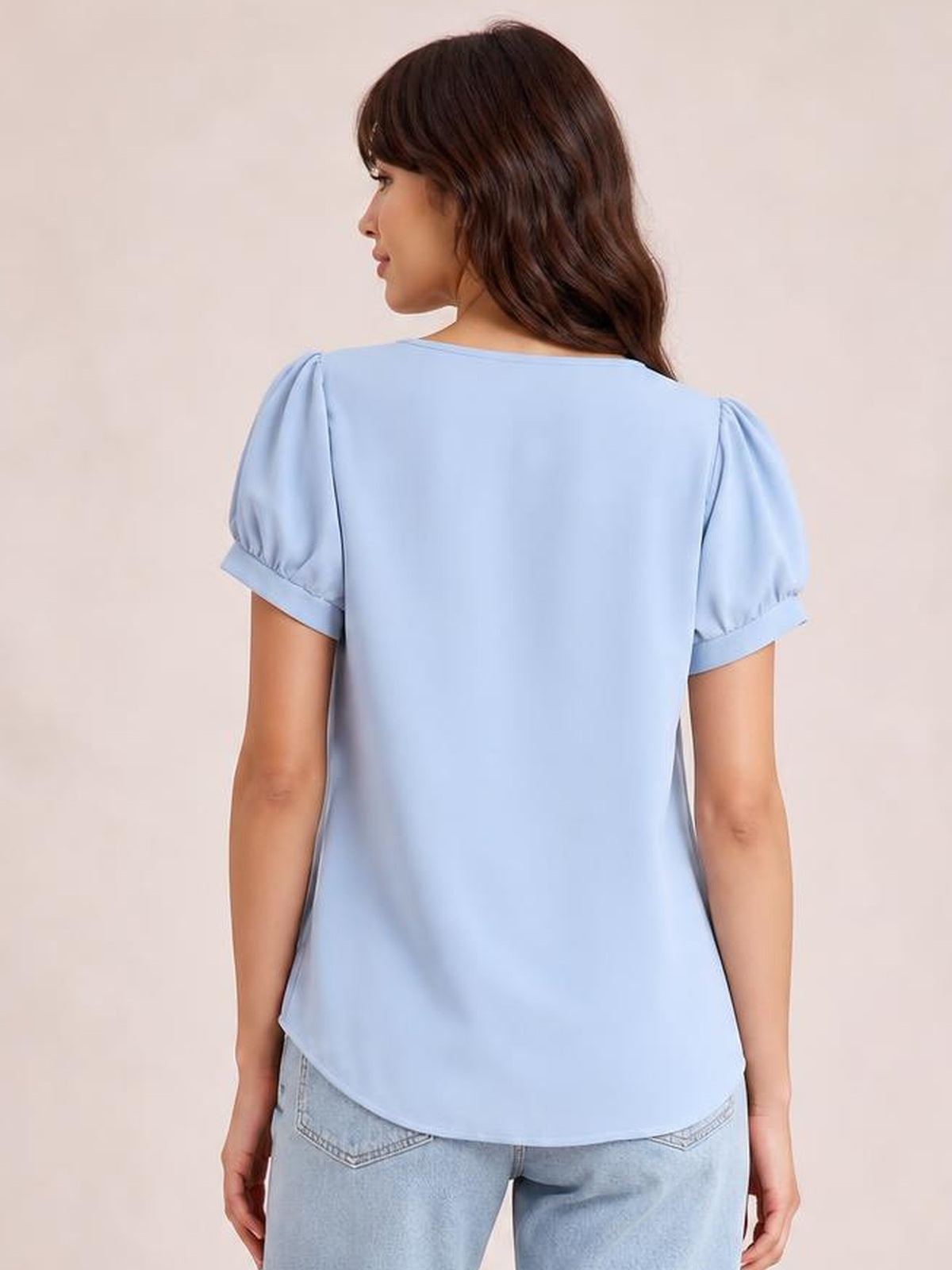 Model shown from behind wearing a light blue short sleeve blouse with puffed shoulders, cuffed sleeves, a relaxed silhouette, and a curved hem.