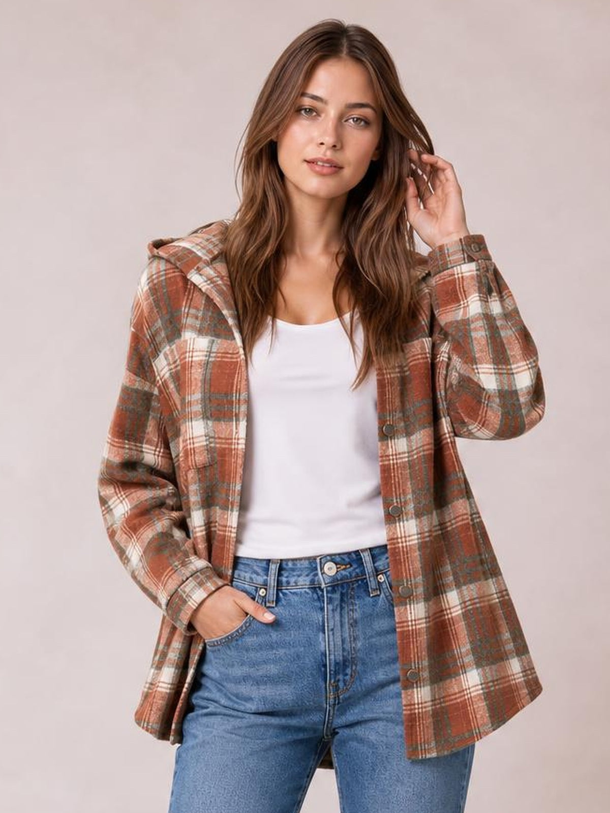 Model wears a rust, cream, and gray plaid button-up hooded jacket with long sleeves, front pockets, and a relaxed hip-length silhouette.