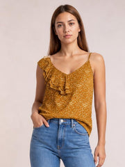 Model poses in a mustard polka dot tank top with a V-neck, spaghetti straps, asymmetrical hem, and cascading ruffle trim.