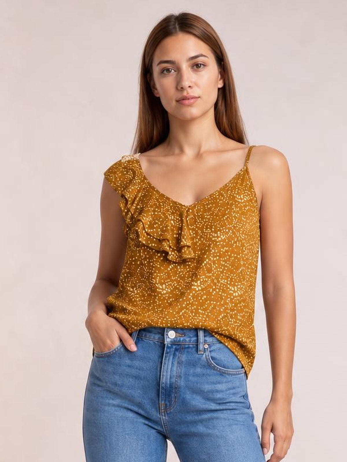 Model poses in a mustard polka dot tank top with a V-neck, spaghetti straps, asymmetrical hem, and cascading ruffle trim.