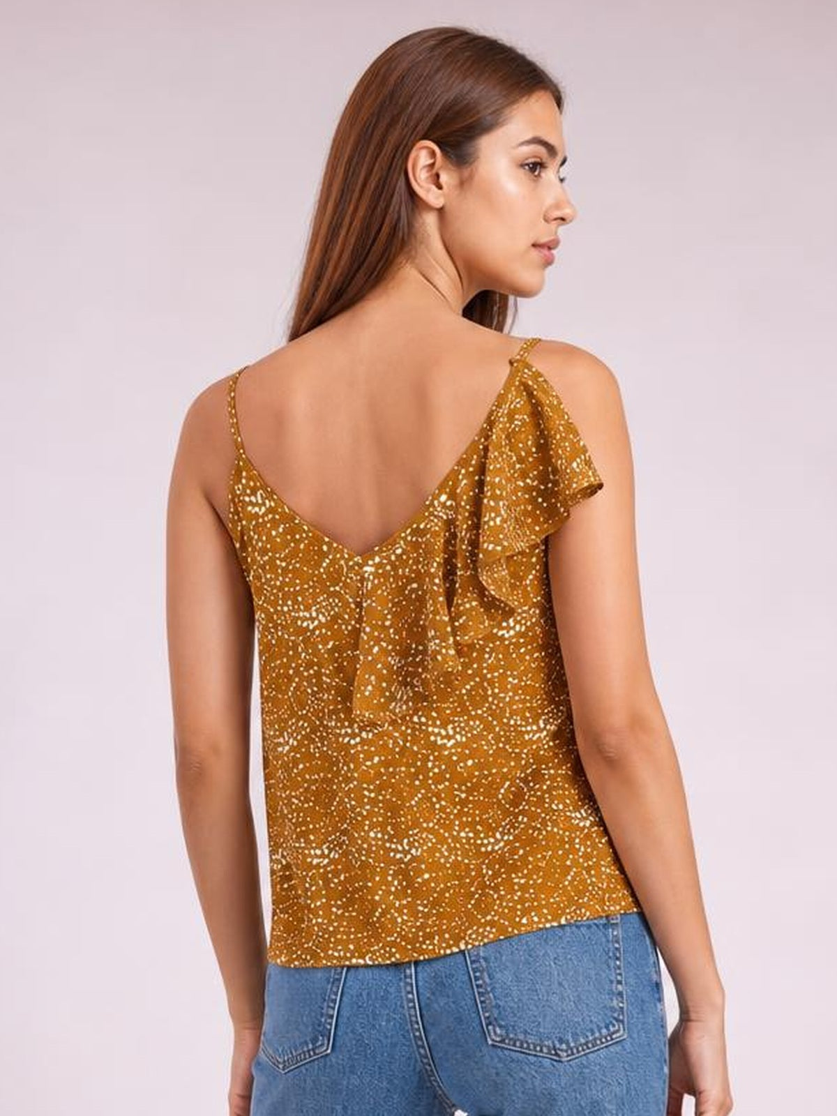 Model shown from the back wearing a mustard-brown polka dot tank top with spaghetti straps, a V-back, asymmetrical ruffle trim, and a straight regular silhouette.