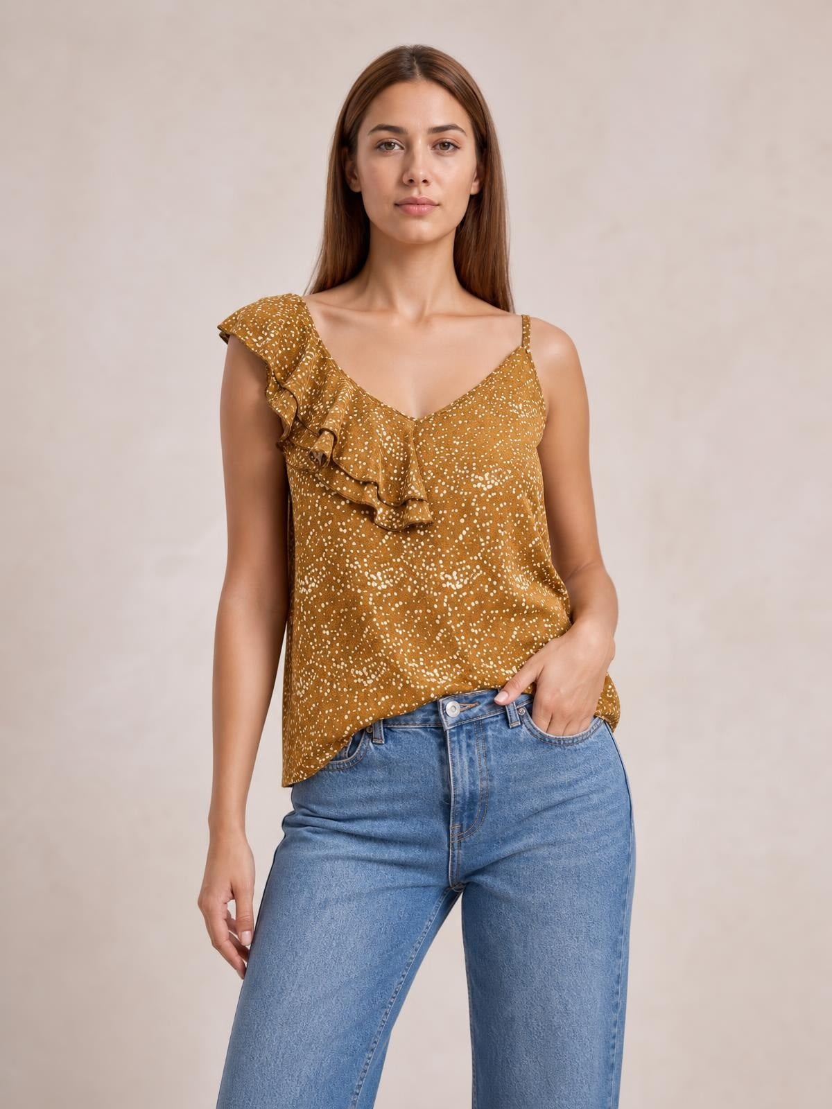 Model wearing a mustard polka dot asymmetrical tank top with a V-neck, spaghetti straps, sleeveless cut, and layered ruffle trim.
