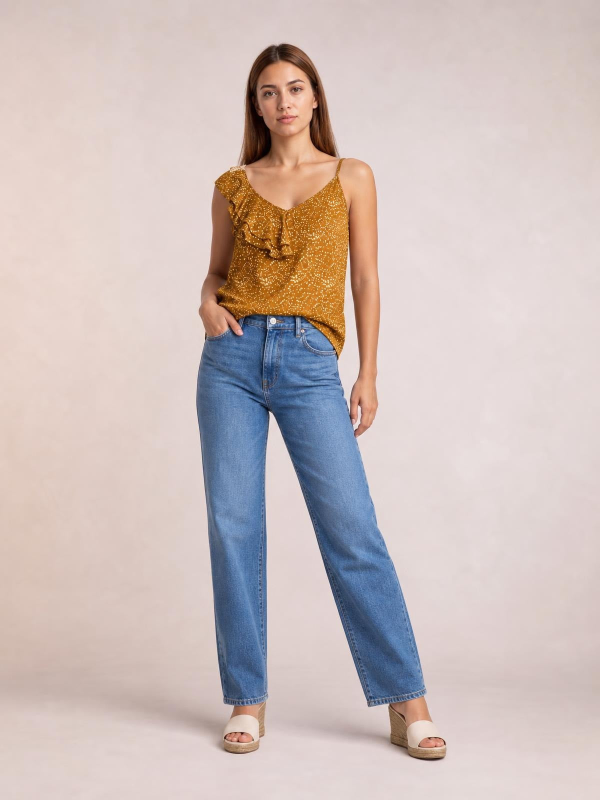 Model wearing a mustard polka dot asymmetrical tank top with a V-neck, spaghetti straps, ruffle trim, and a relaxed silhouette.