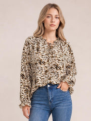 Model wears a long printed blouse with a tie neck, frill trim, and flounce sleeves in a beige, brown, and black animal-inspired pattern.